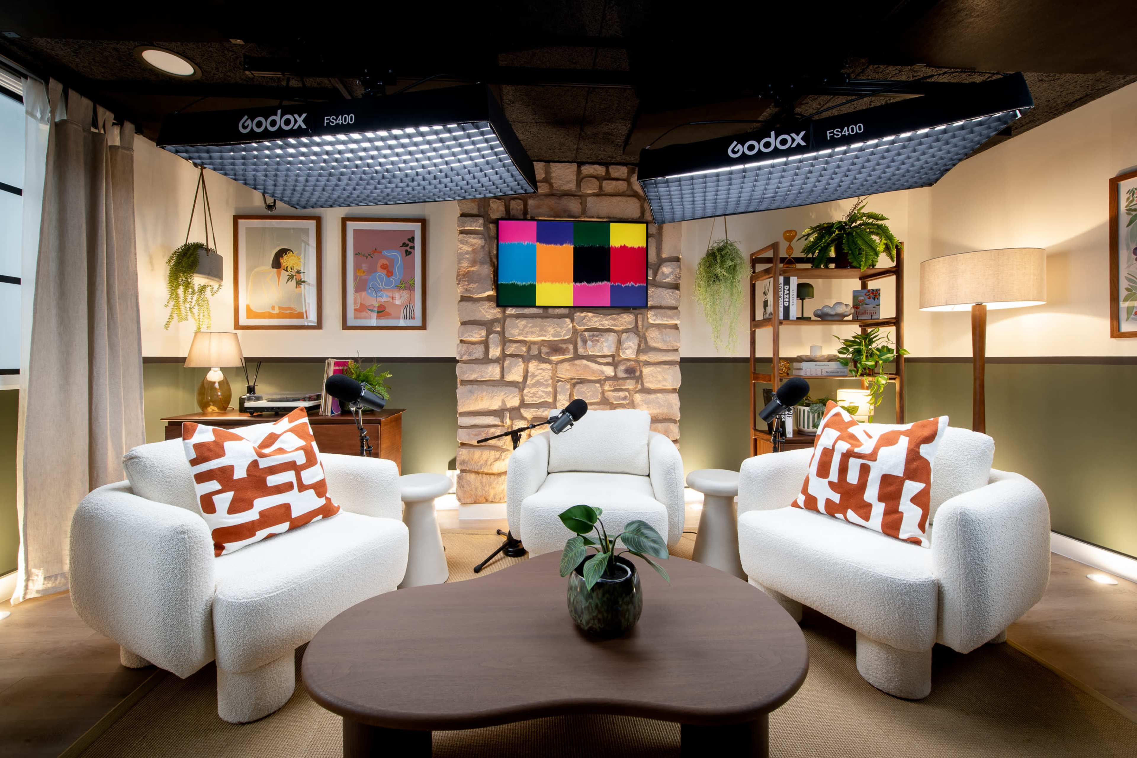 The image shows a cozy, modern indoor setting with two white, textured chairs positioned around a round wooden table, framed by stone walls and soft lighting.