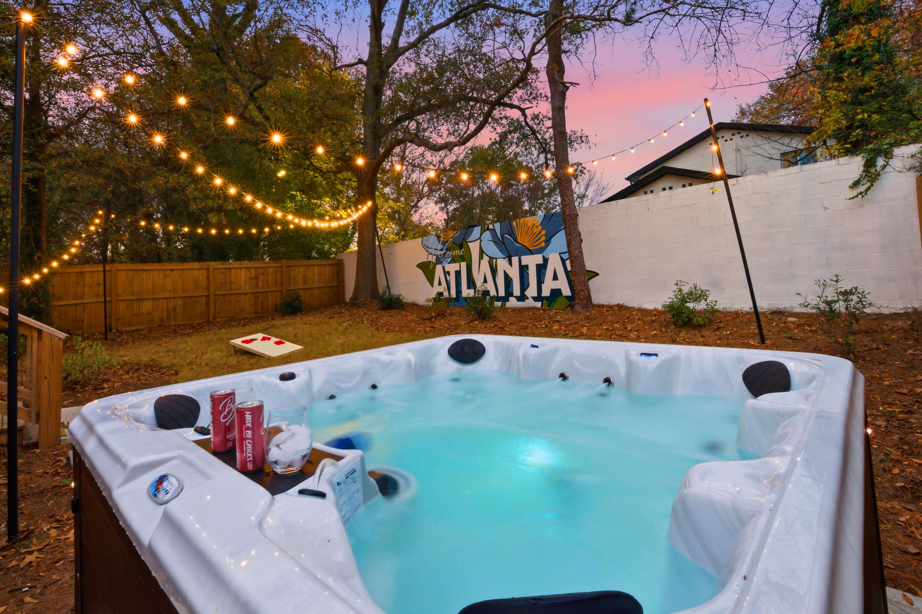 A hot tub sits in a backyard adorned with string lights and a large mural that reads "ATLANTA."