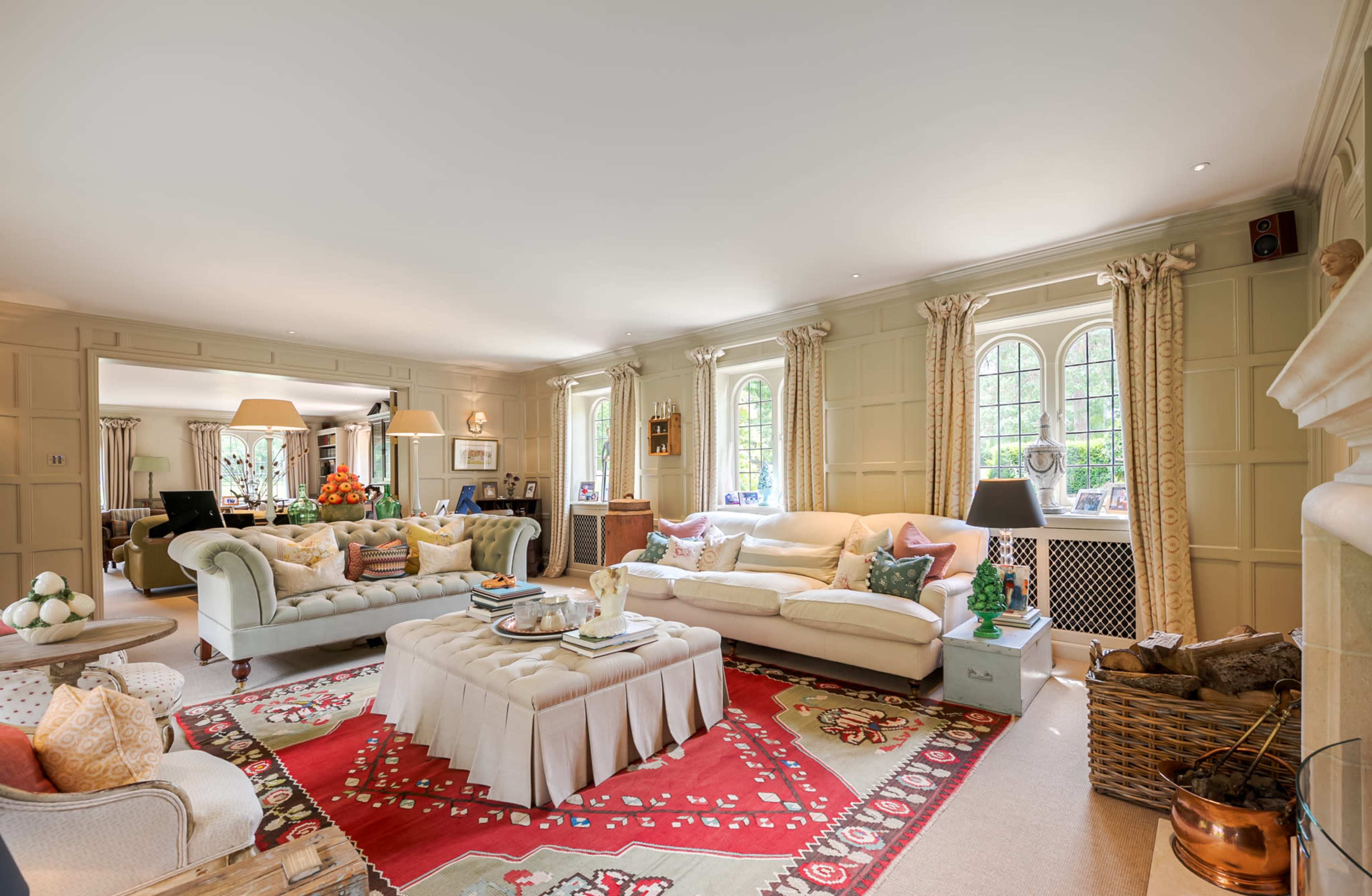A spacious living room featuring a large sectional sofa, a decorative coffee table, and a vibrant area rug, all arranged around windows that allow natural light to fill the space.
