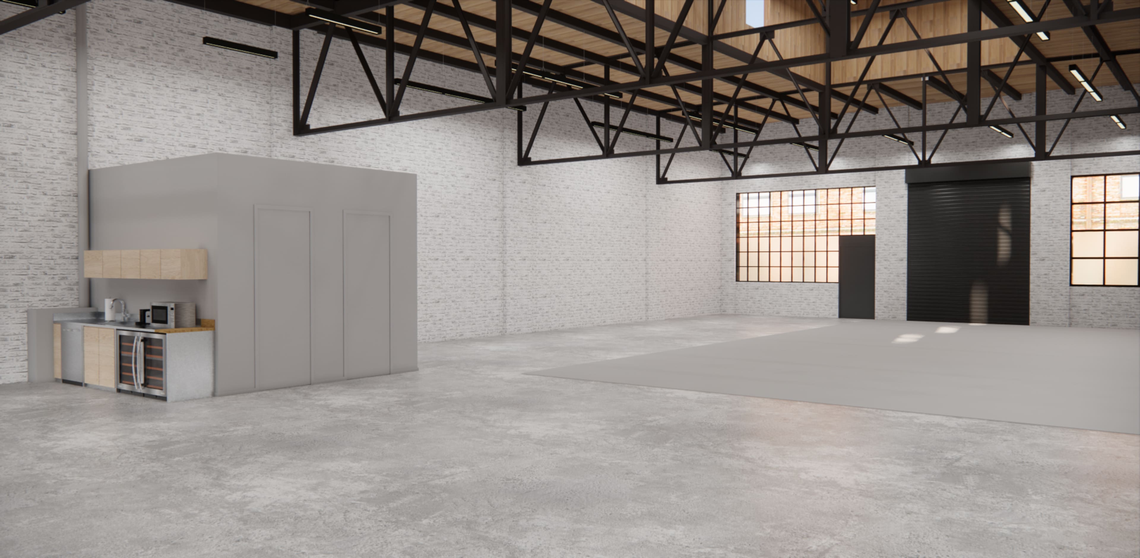 An open industrial space with exposed brick walls, large windows, and a kitchen area on one side.