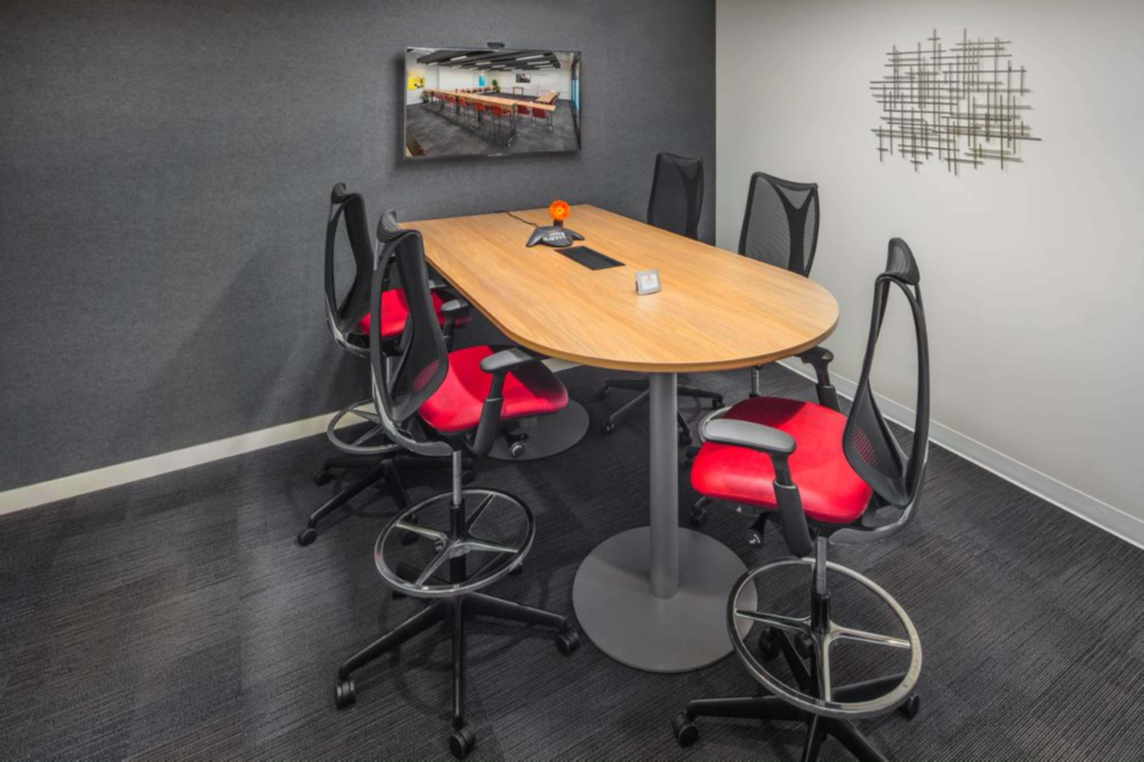A conference room with a large oval wooden table surrounded by several high-backed chairs, a wall-mounted television, and a modern wall decoration.