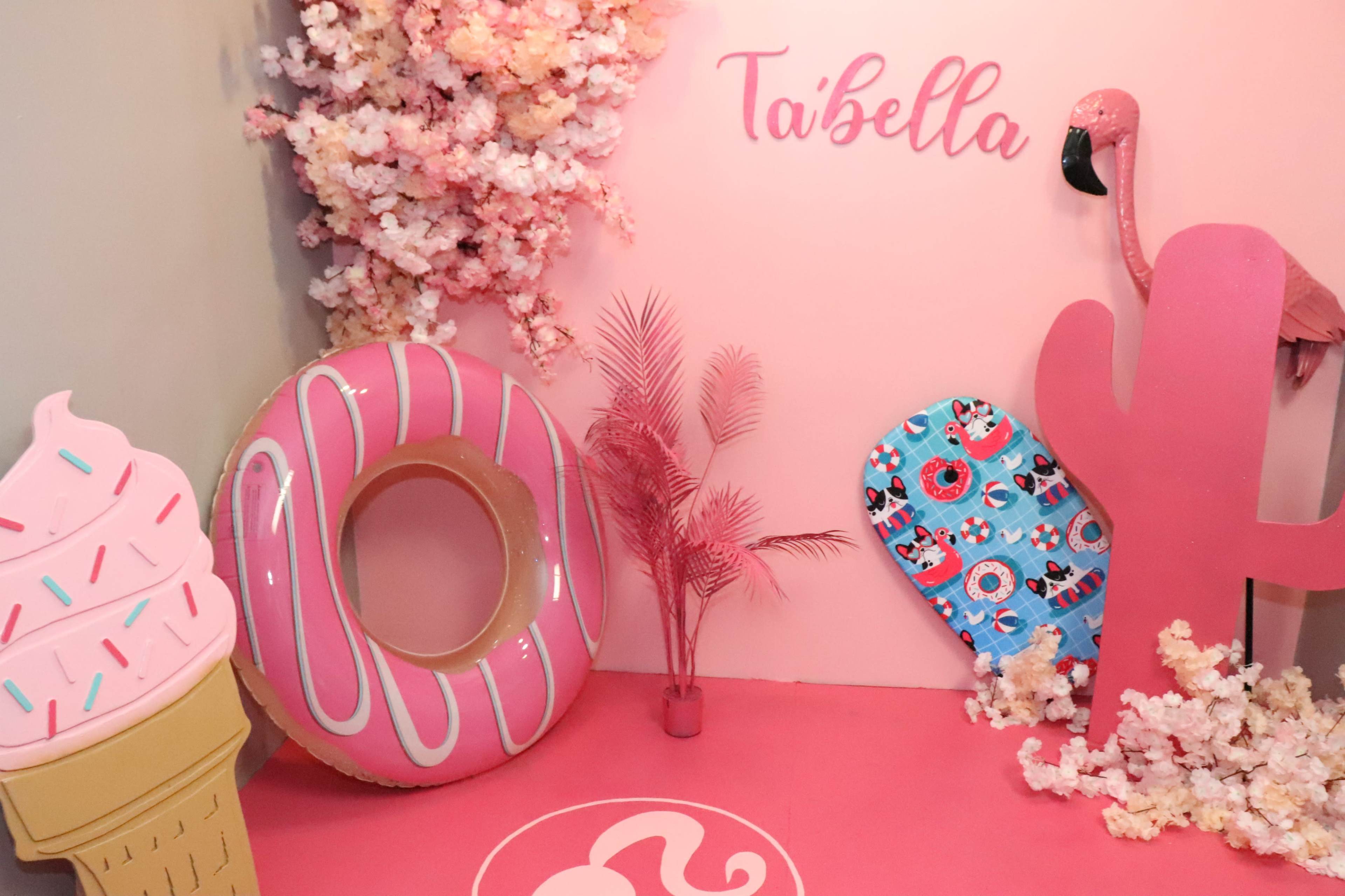 A vibrant pink-themed display featuring oversized props, including an ice cream cone, a donut, a flamingo, a cactus, and tropical leaves.