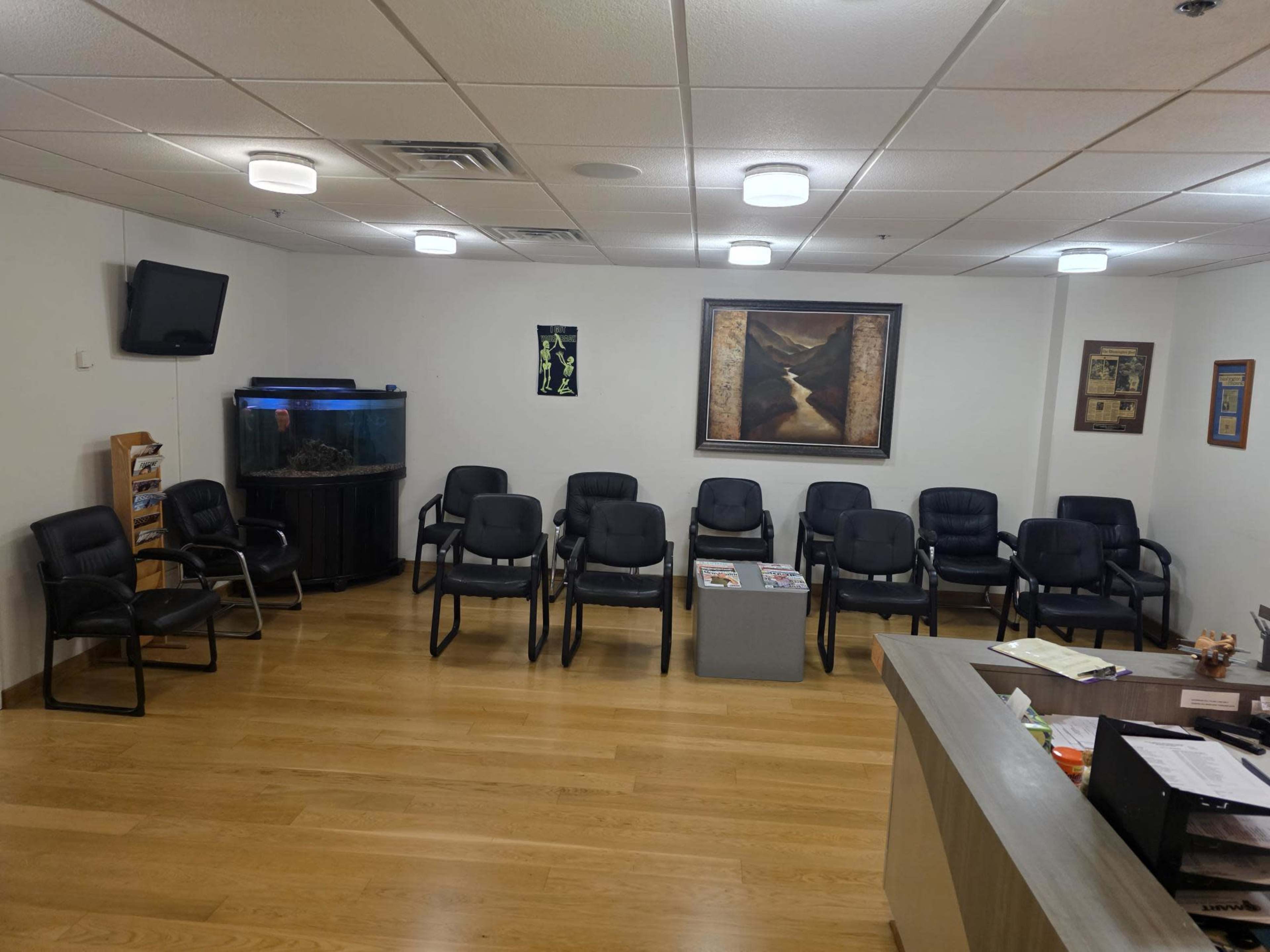 The image shows a waiting room with several black chairs, a fish tank, a painting on the wall, and a reception desk.