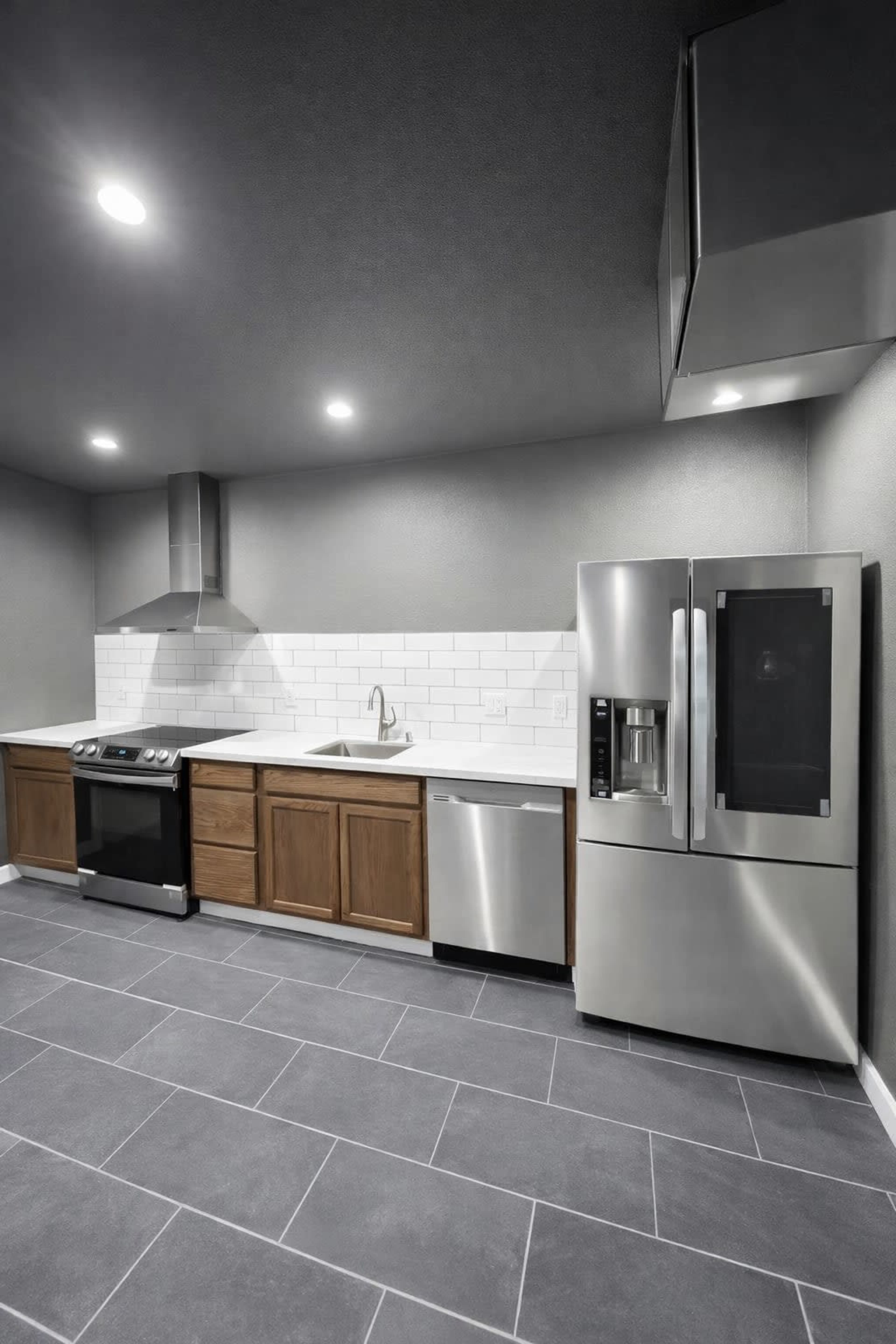 The image shows a modern kitchen featuring stainless steel appliances, brown wooden cabinetry, and a white tiled backsplash against gray walls and flooring.