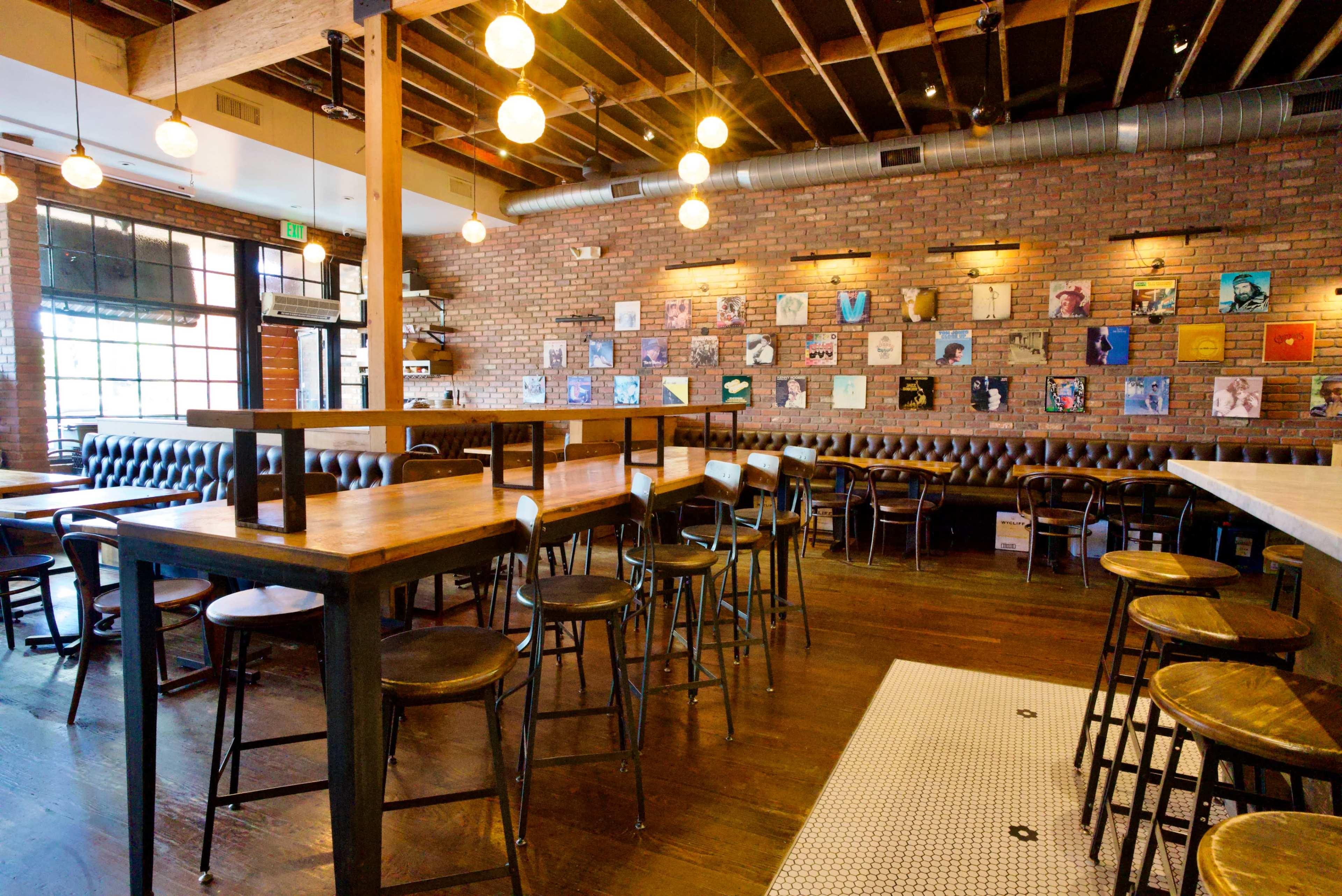 The image shows a modern restaurant interior with brick walls, wooden tables, and a series of framed artworks displayed on the wall.