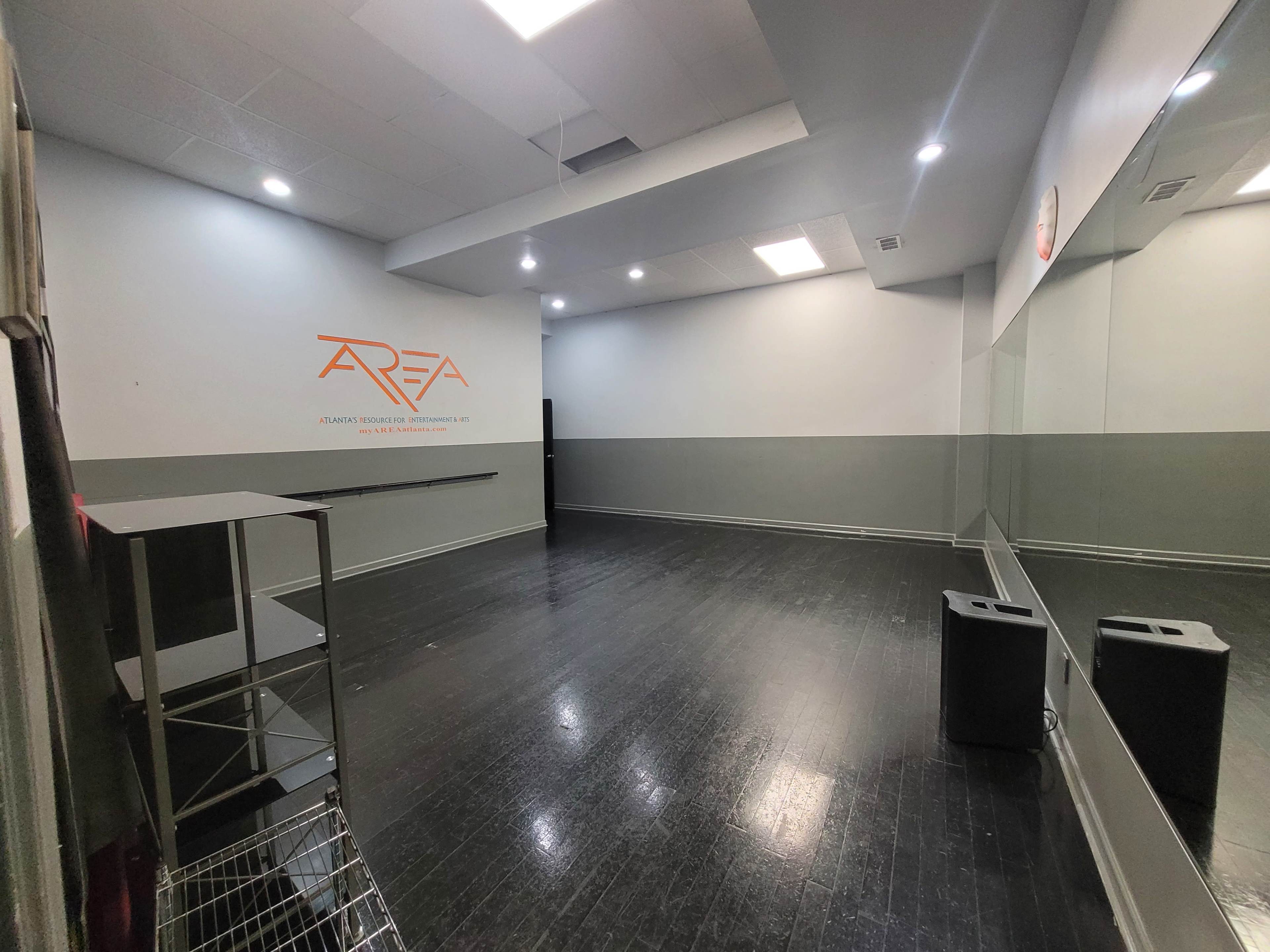 An empty studio space with dark flooring, grey walls, and a large mirror on one side.