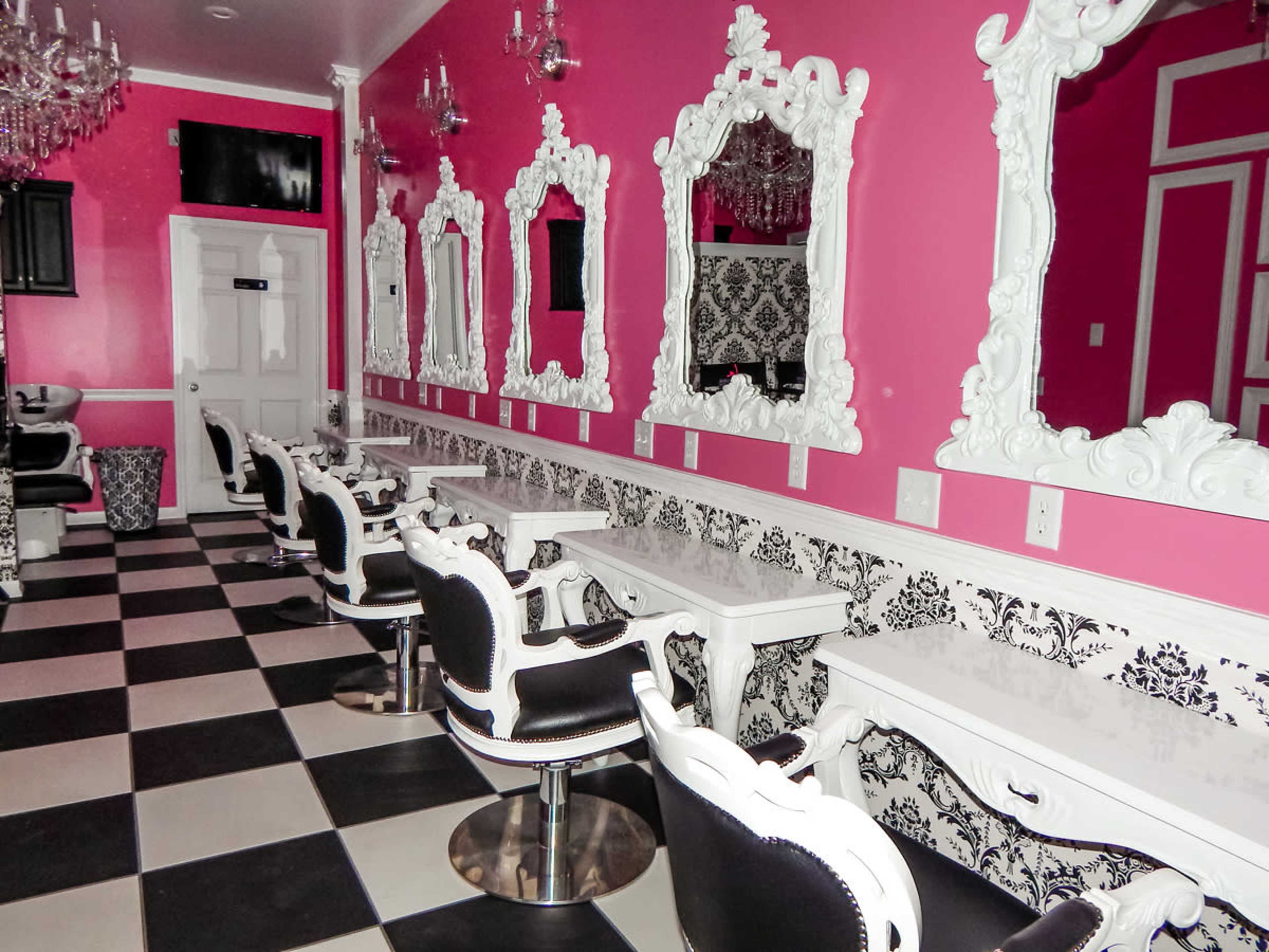 A brightly colored salon interior with pink walls, black and white checkered flooring, and ornate white-framed mirrors along the wall.