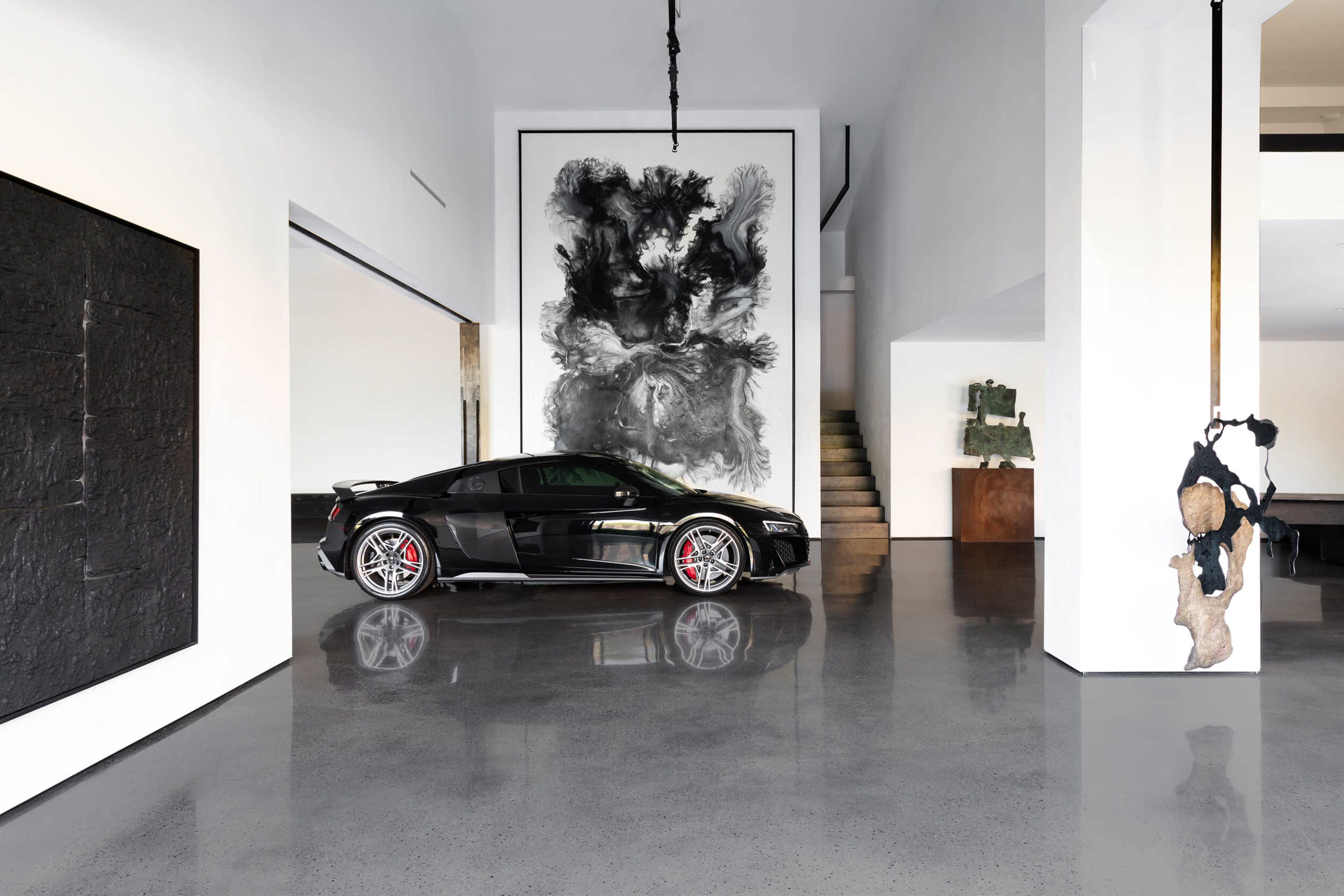 A black sports car is parked in a modern interior featuring large artworks and polished concrete floors.