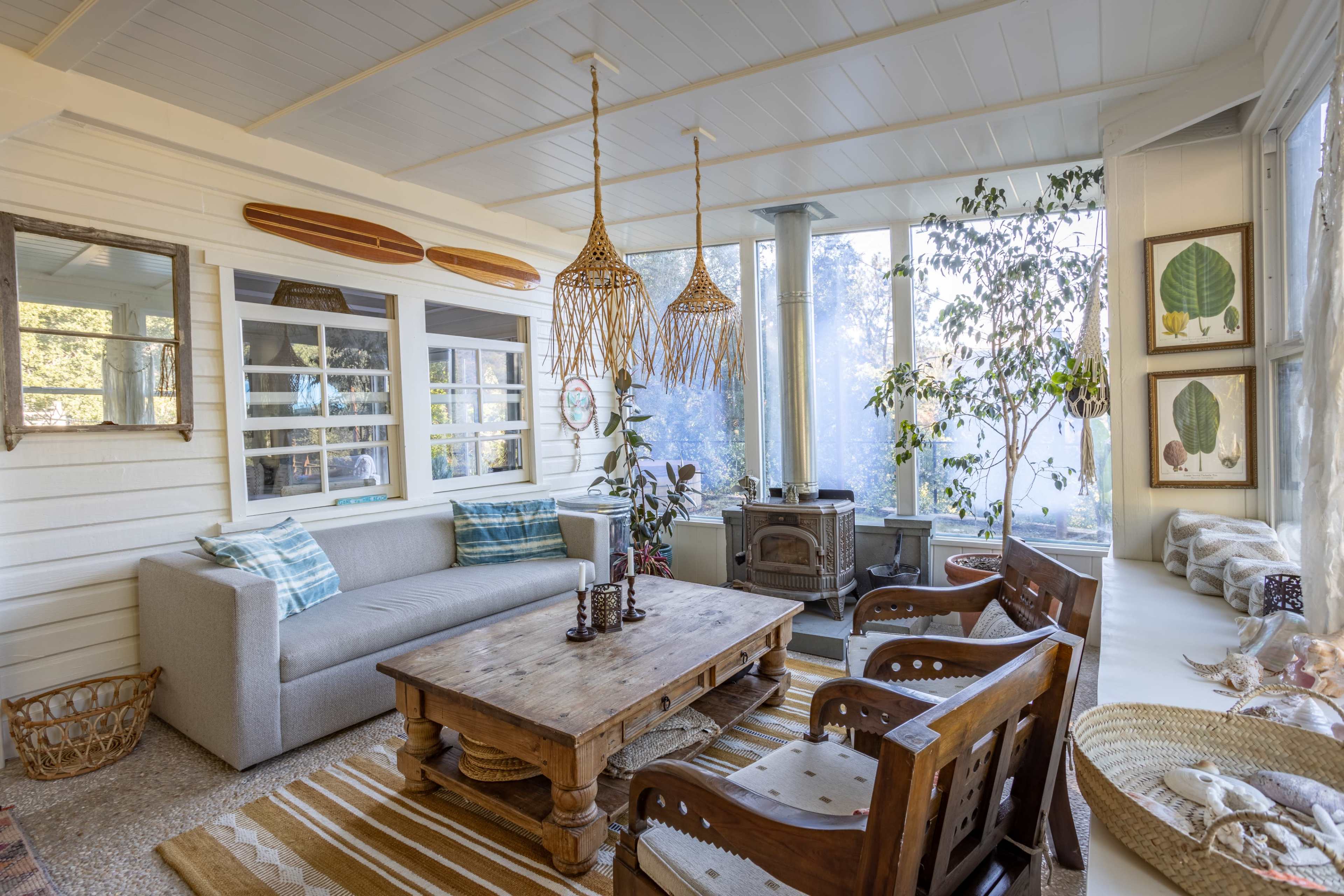 A bright sunroom with a gray sofa, a wooden coffee table, and several windows allowing natural light to enter.