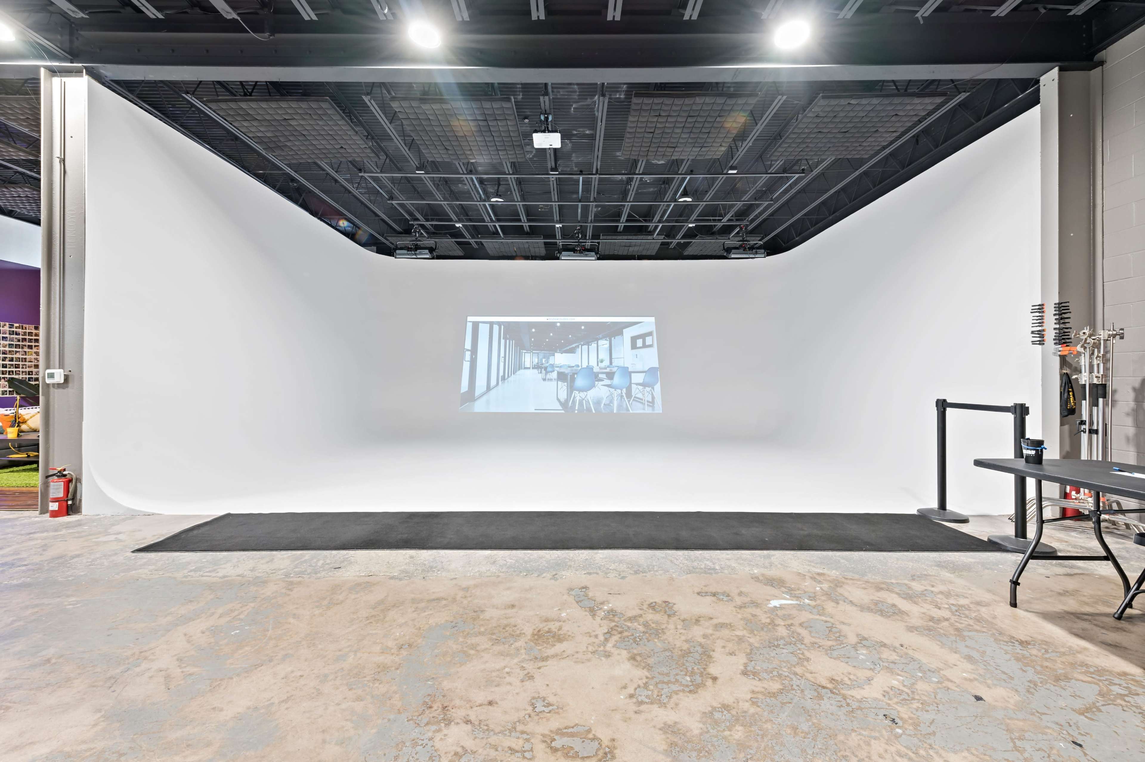 A spacious studio features a white backdrop with a projected grayscale image of an interior space.