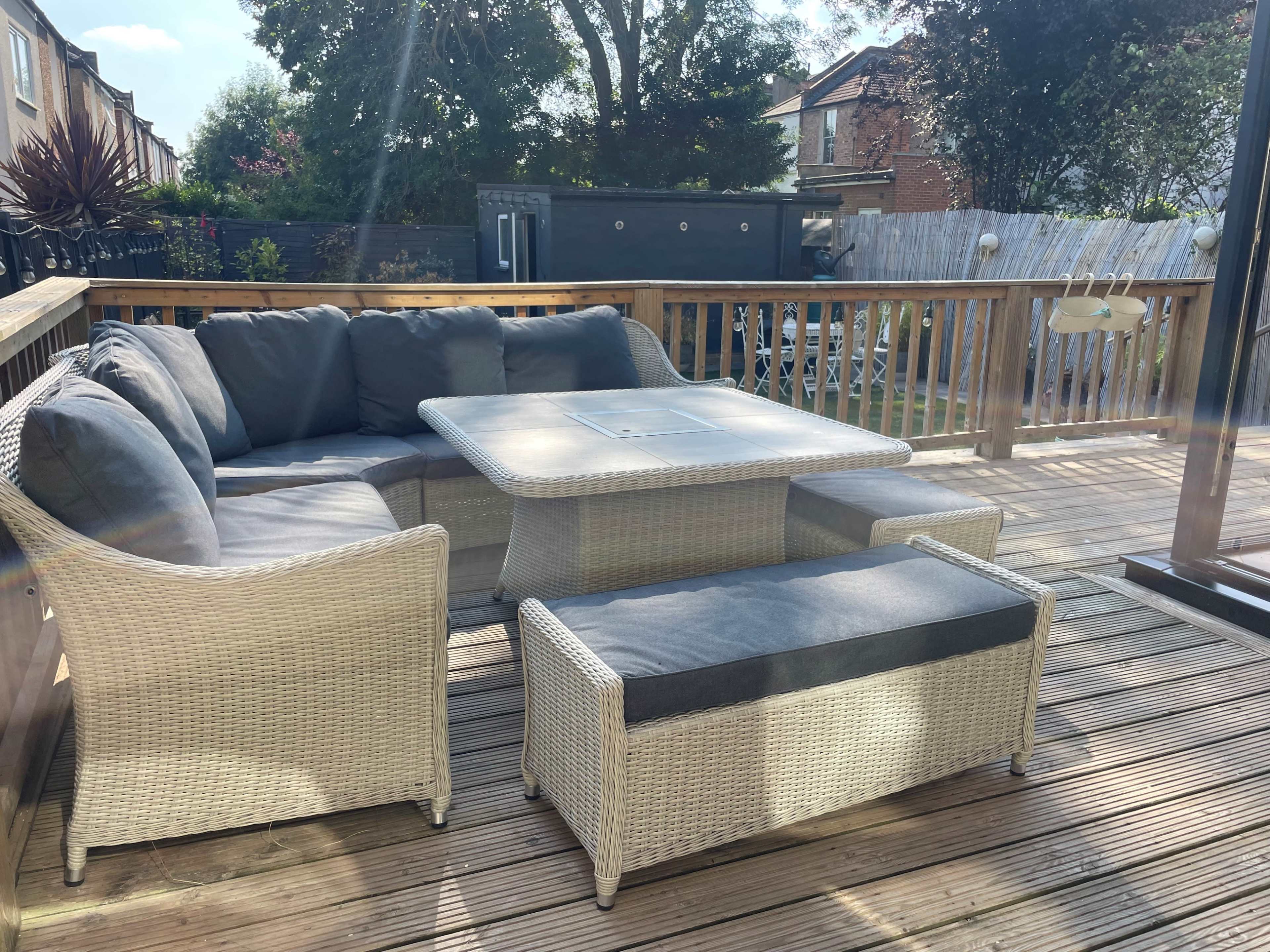 A patio area with a sectional sofa, a coffee table, and additional seating on a wooden deck surrounded by greenery.