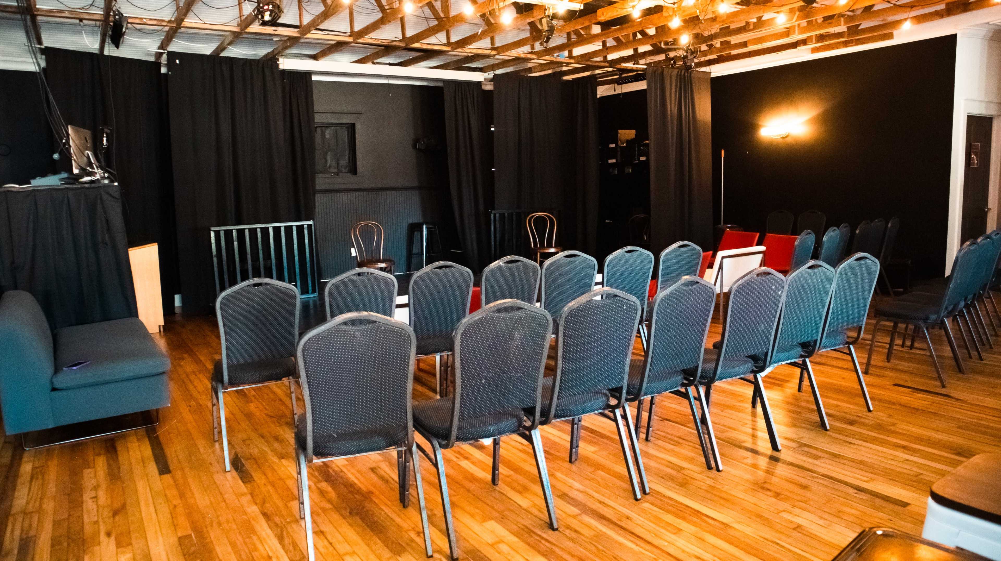 A performance space features rows of chairs set up in a circular arrangement with black curtains and wooden flooring.