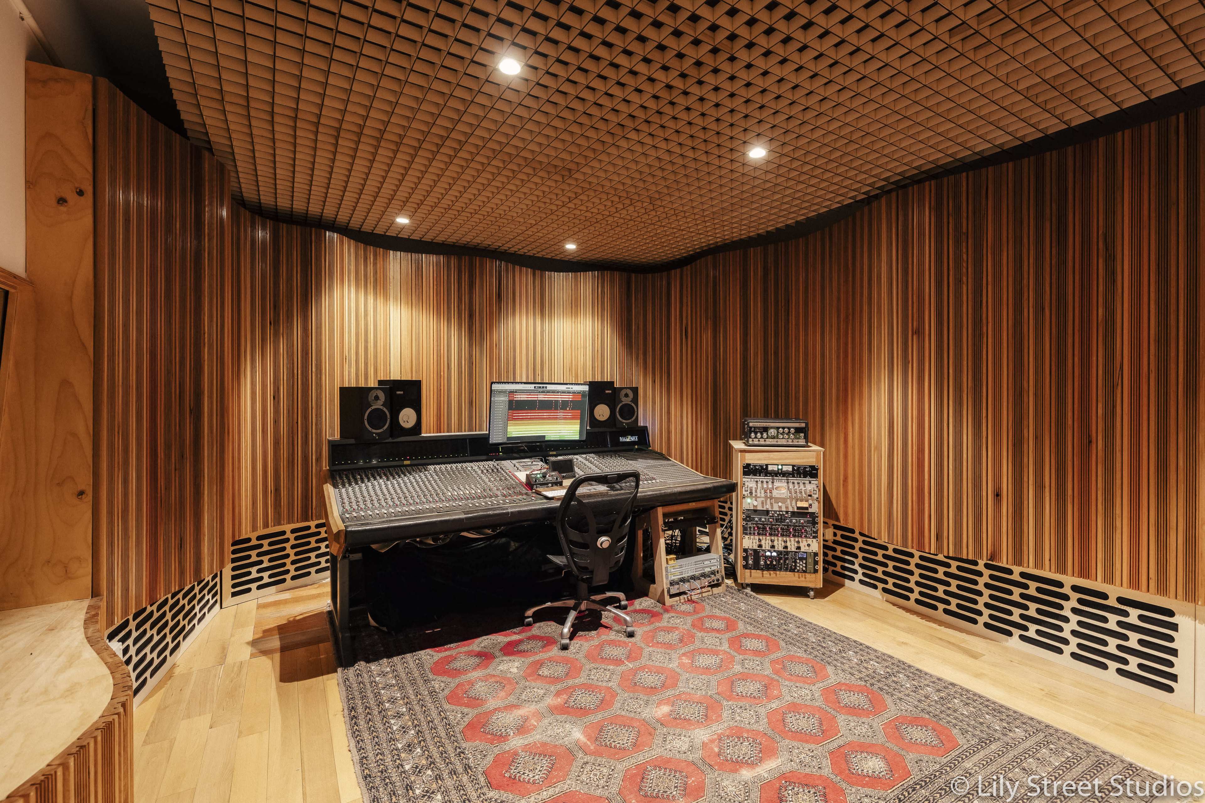 A music studio features a wooden-paneled interior with a central mixing desk, speakers, and electronic equipment.
