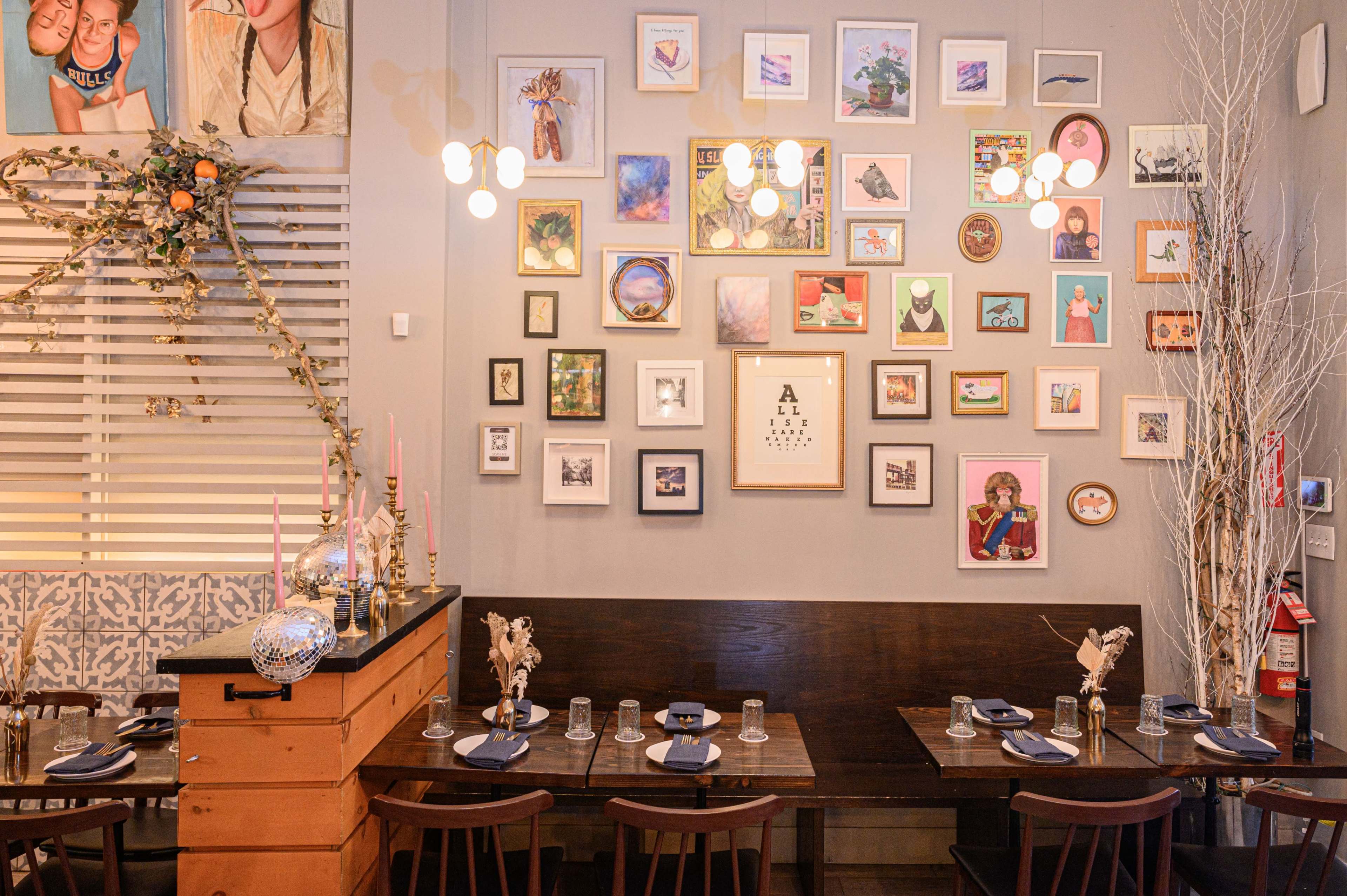 A dining area features wooden tables set with plates and glasses, against a wall adorned with an array of framed pictures and artwork.