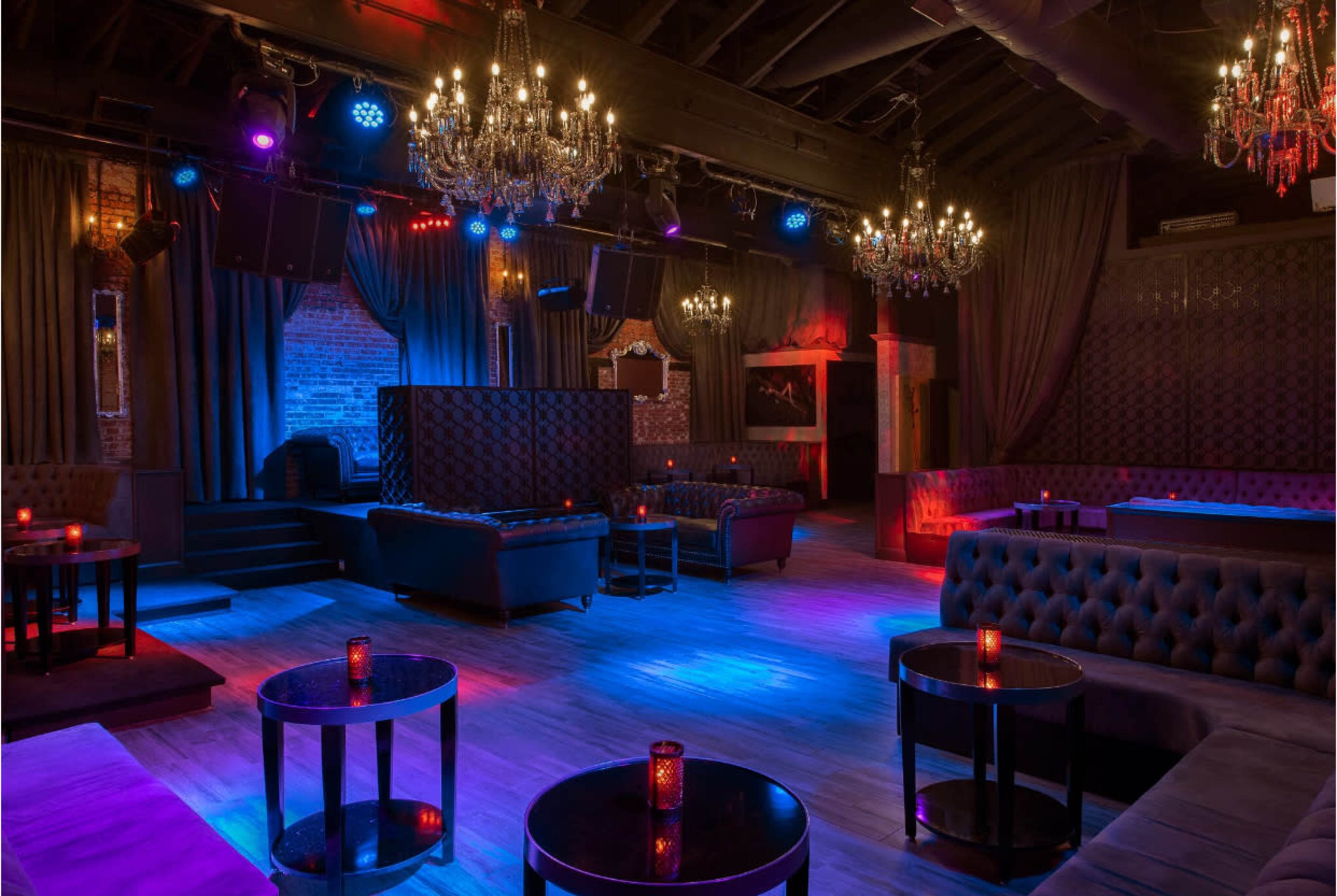 The image shows a dimly lit nightclub with plush seating, ornate chandeliers, and colored lighting casting a vibrant ambiance.