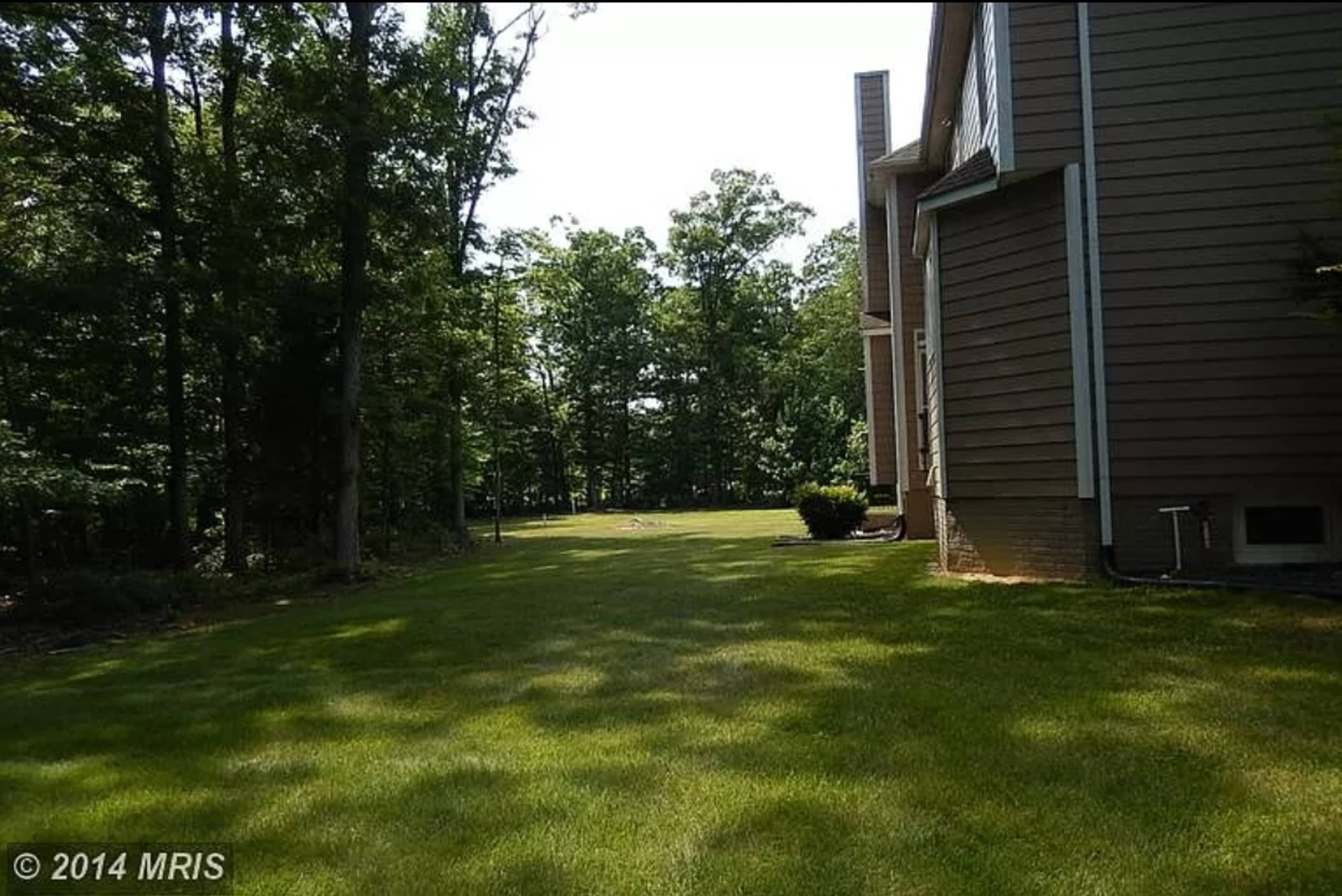 A grassy yard surrounded by trees next to a residential structure.
