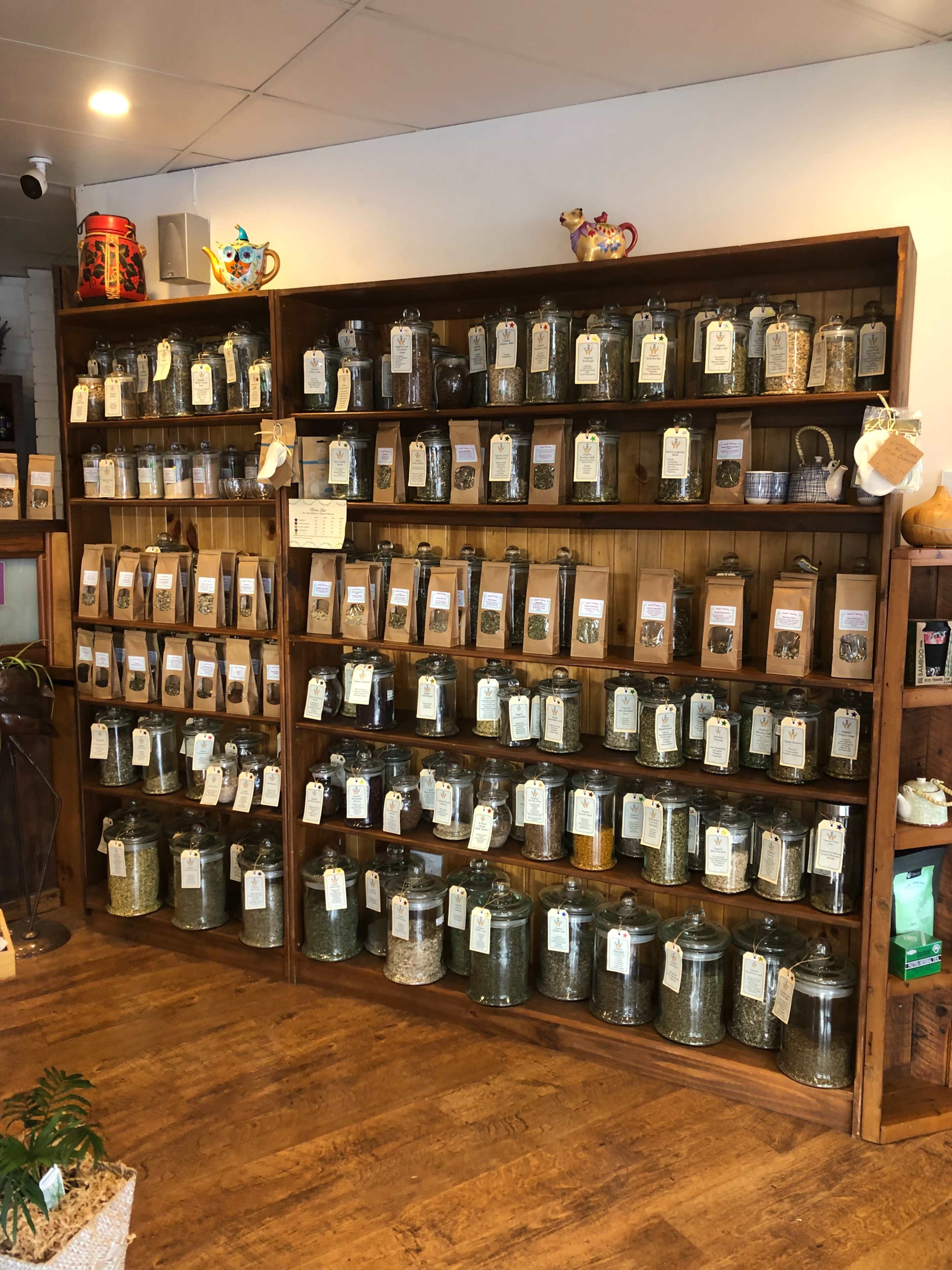 A wooden shelving unit displays numerous jars filled with herbs and spices, each labeled for identification.