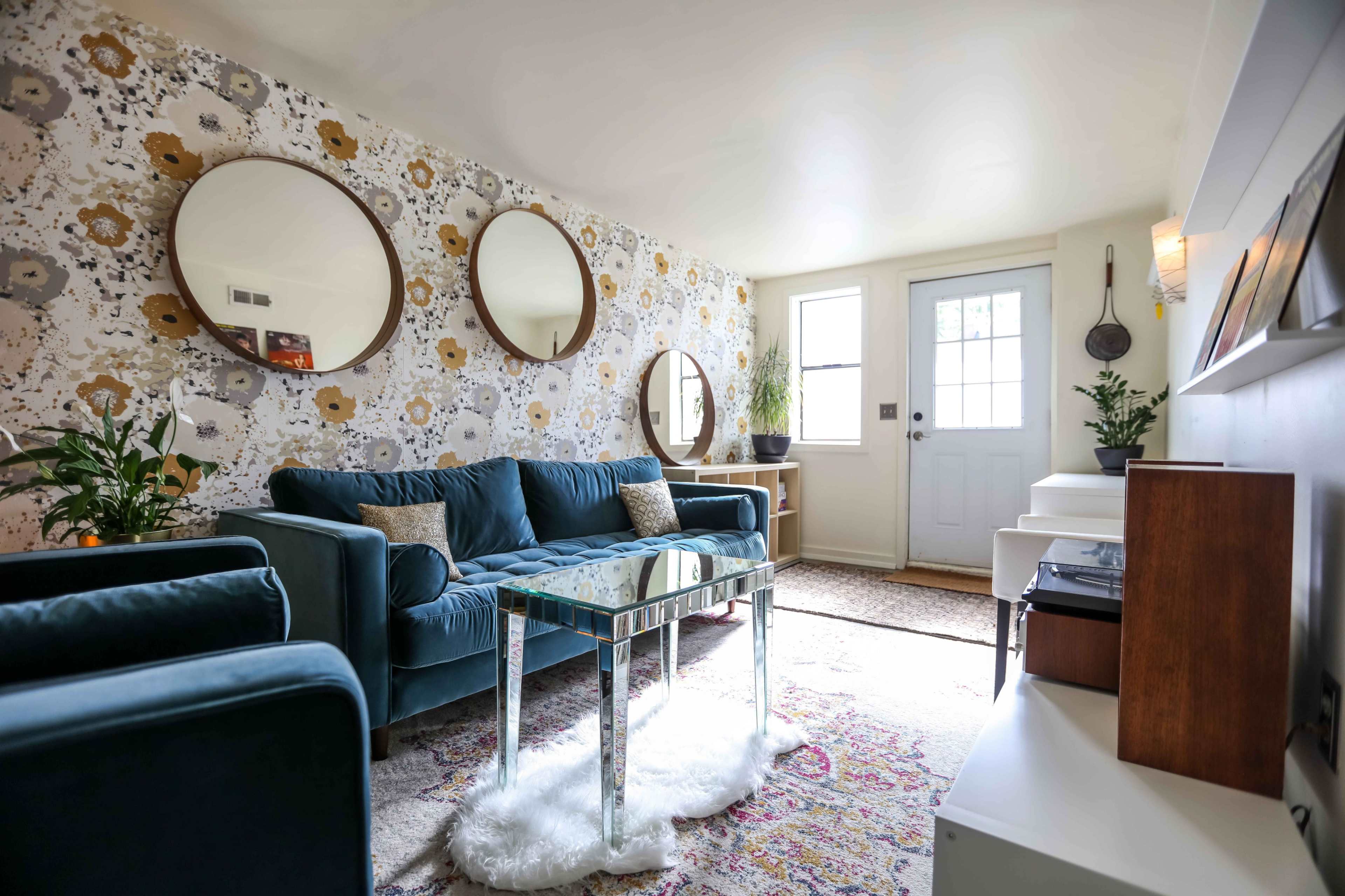 The living room features a teal sofa, three round mirrors on the patterned wallpaper, and a glass coffee table on a colorful area rug.