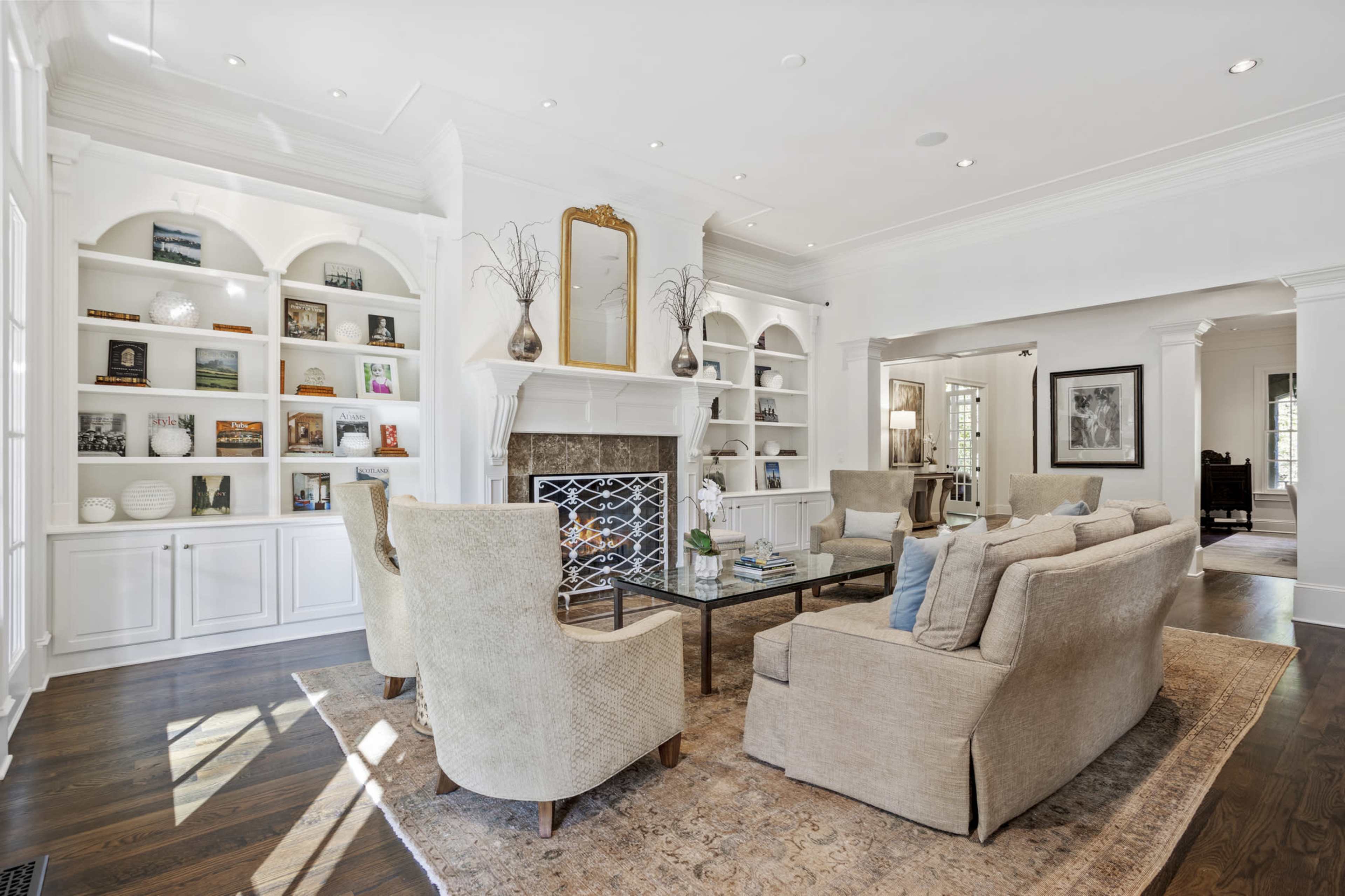 A spacious living room with a fireplace, bookshelves, and a seating arrangement featuring beige sofas and armchairs.