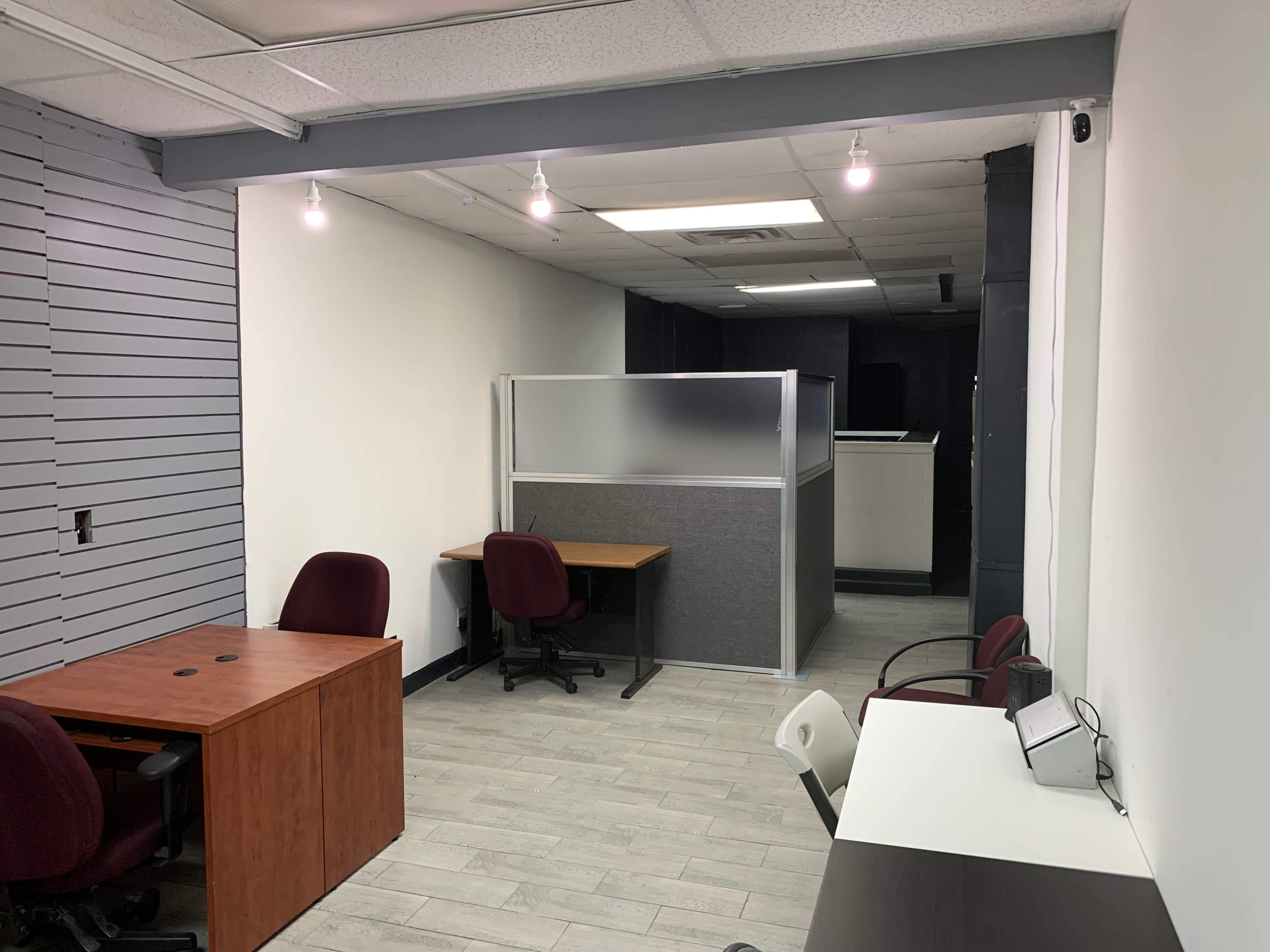 An office space with two wooden desks, chairs, and a partial partition dividing different areas.