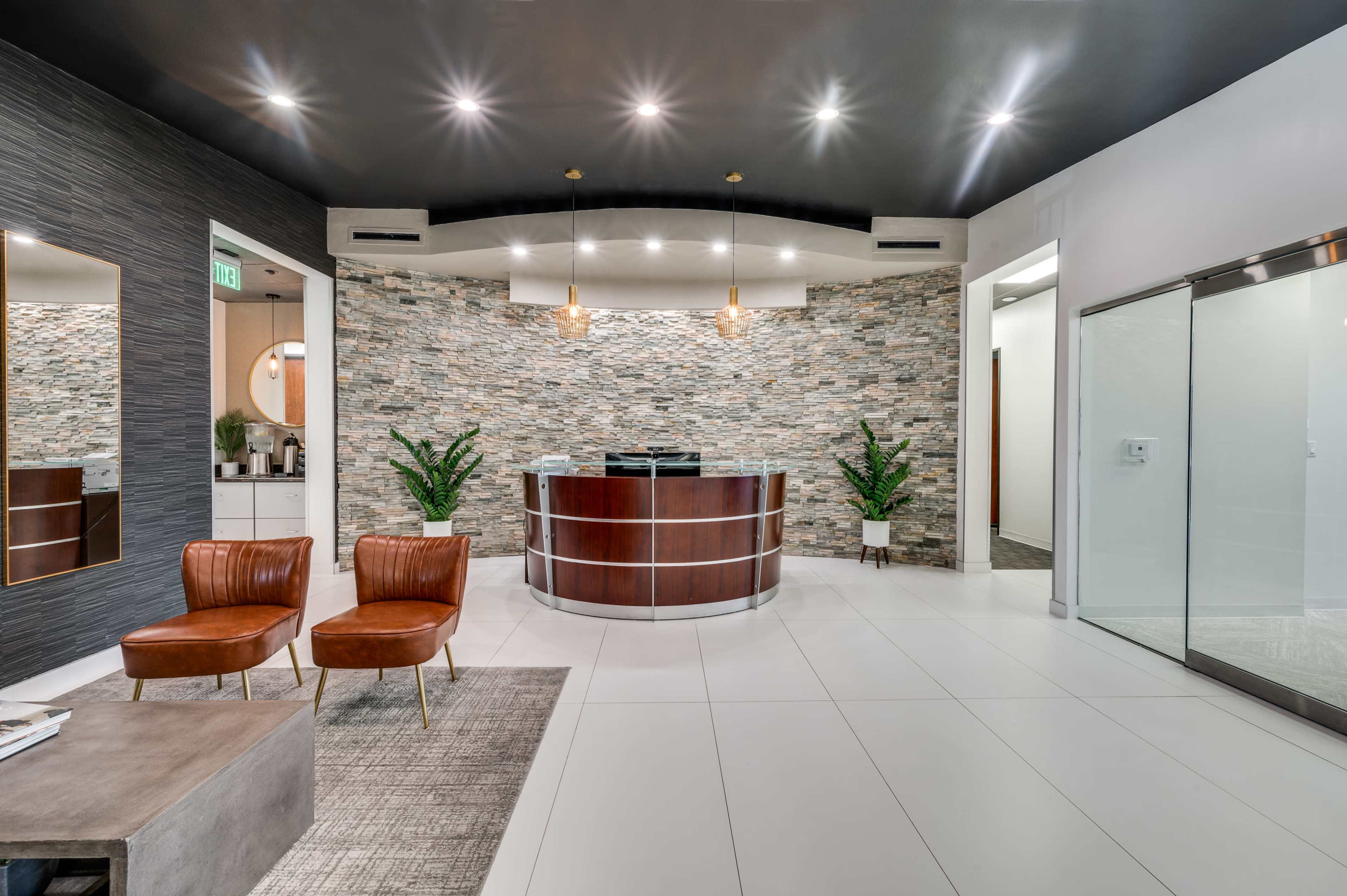 The image shows a modern reception area with a stone feature wall, two leather chairs, and a glass door leading to another room.