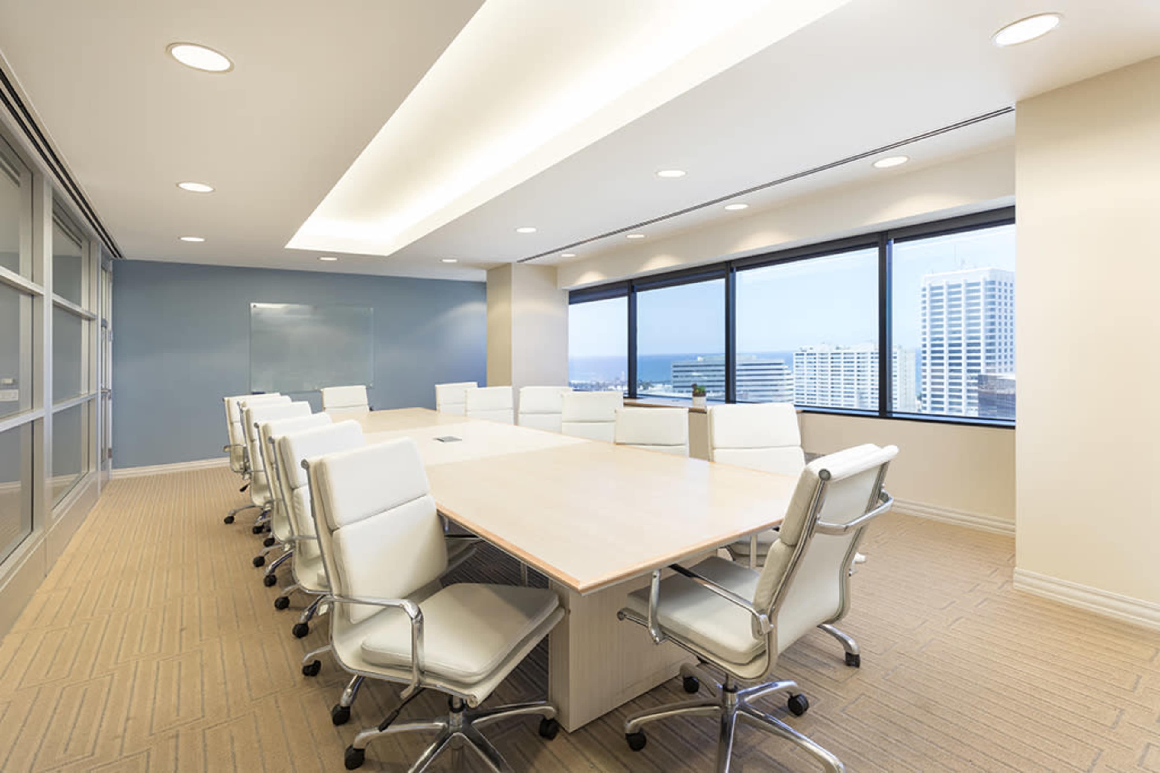 A large conference room features a long wooden table surrounded by white leather chairs, with windows displaying a cityscape.