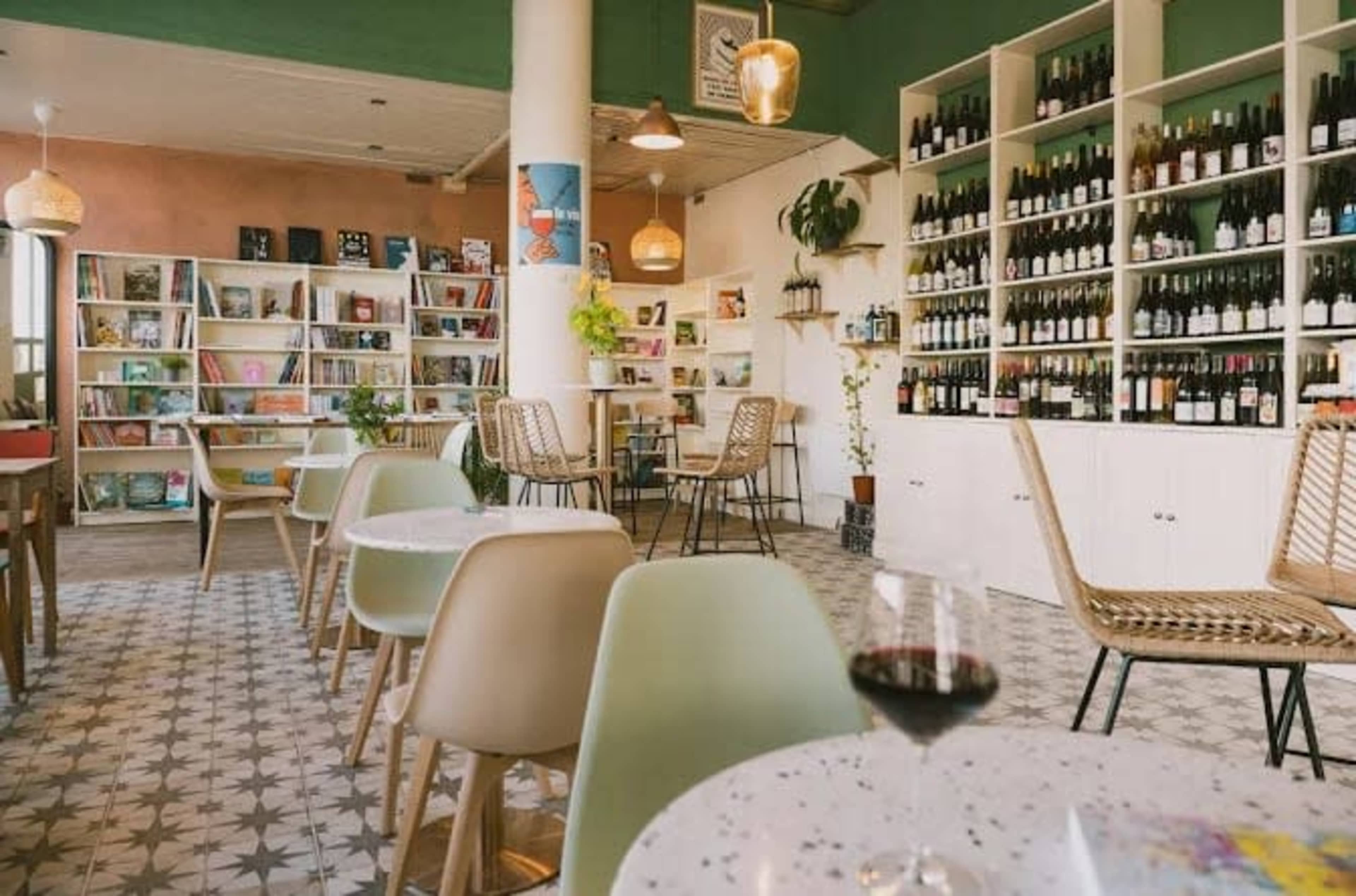 The image shows a cozy café interior with wooden bookshelves filled with wine bottles, tables with chairs, and a decorative layout.