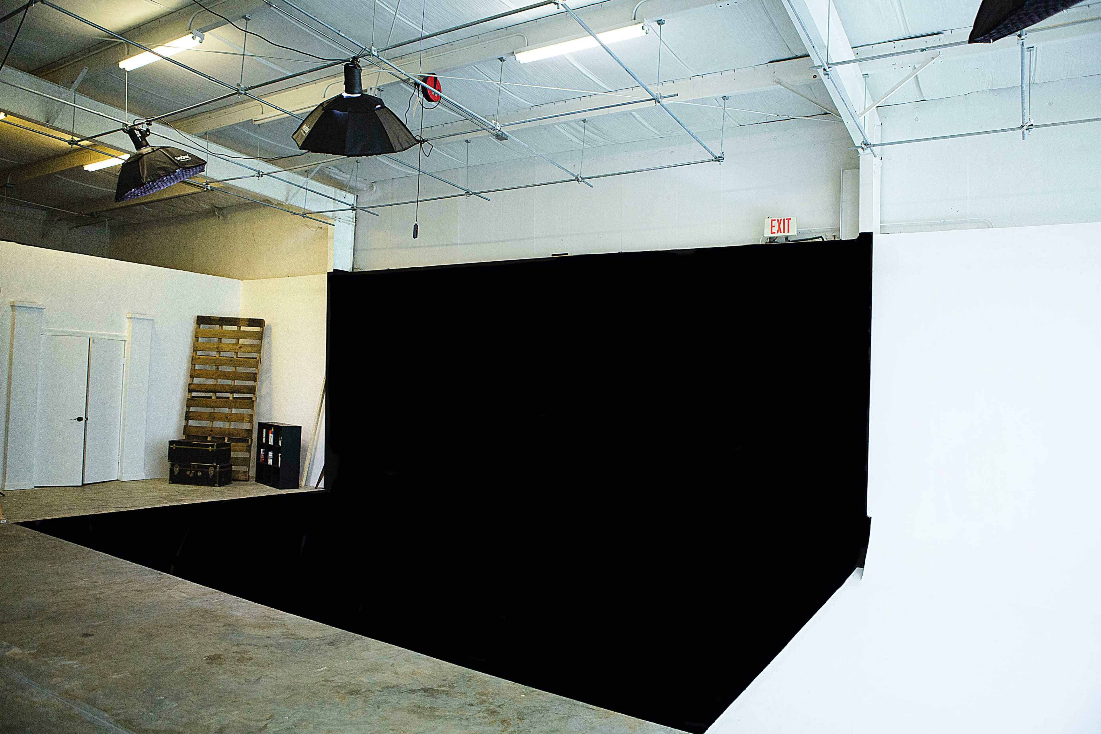 A spacious studio with a black backdrop, concrete flooring, and various lighting fixtures hanging from the ceiling.