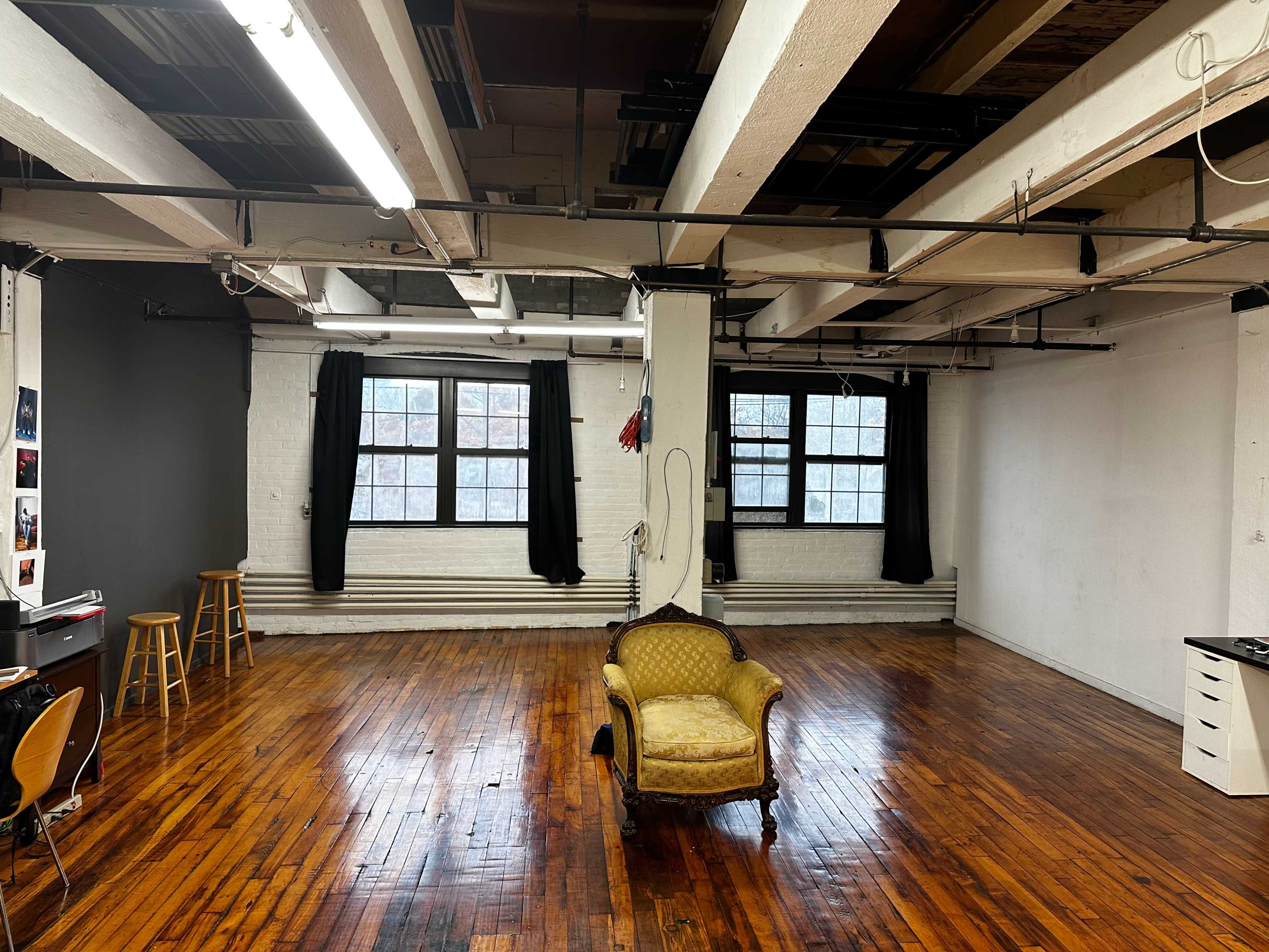 A spacious room with wooden floors, large windows, and a vintage armchair in the center.