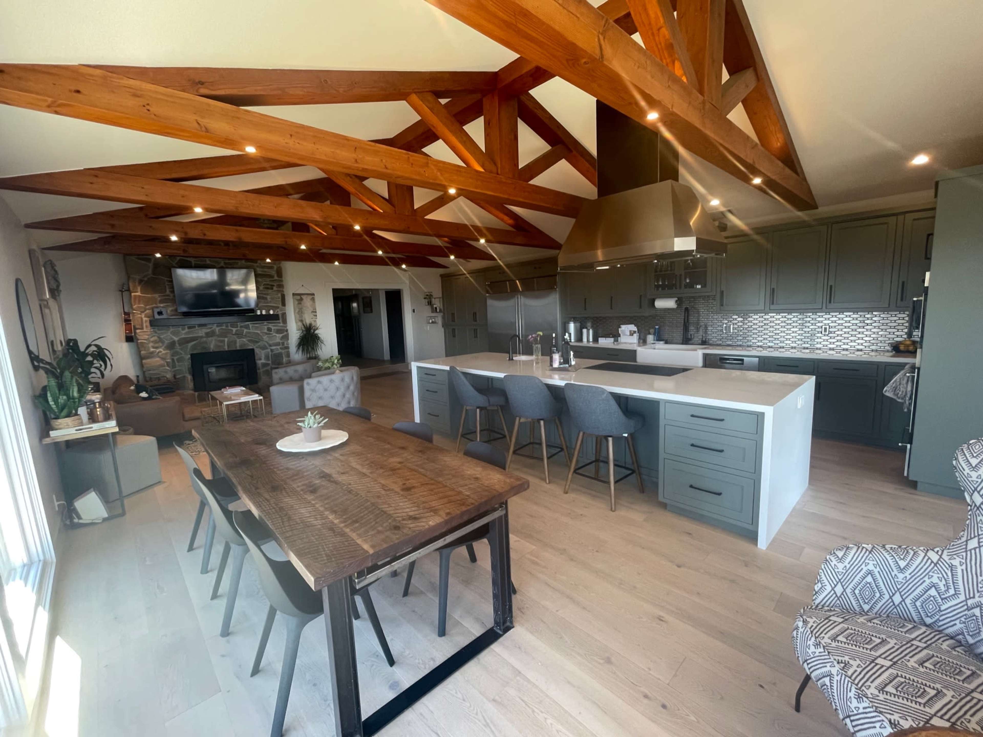 A spacious modern kitchen and dining area featuring wooden beams, a large island with seating, and a rustic dining table.