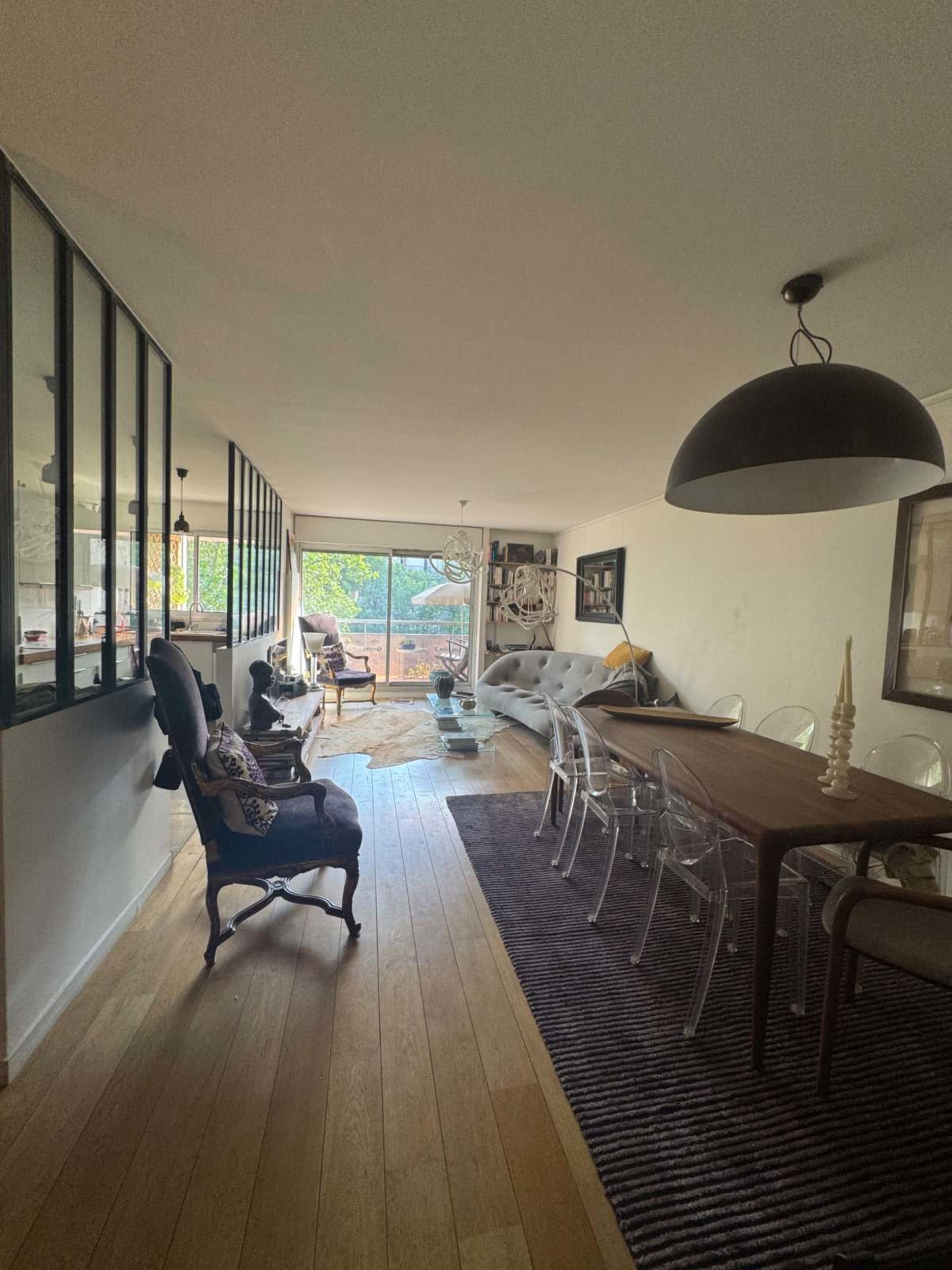 The image shows a modern living and dining area with wooden floors, large windows, and a mix of contemporary and traditional furniture.