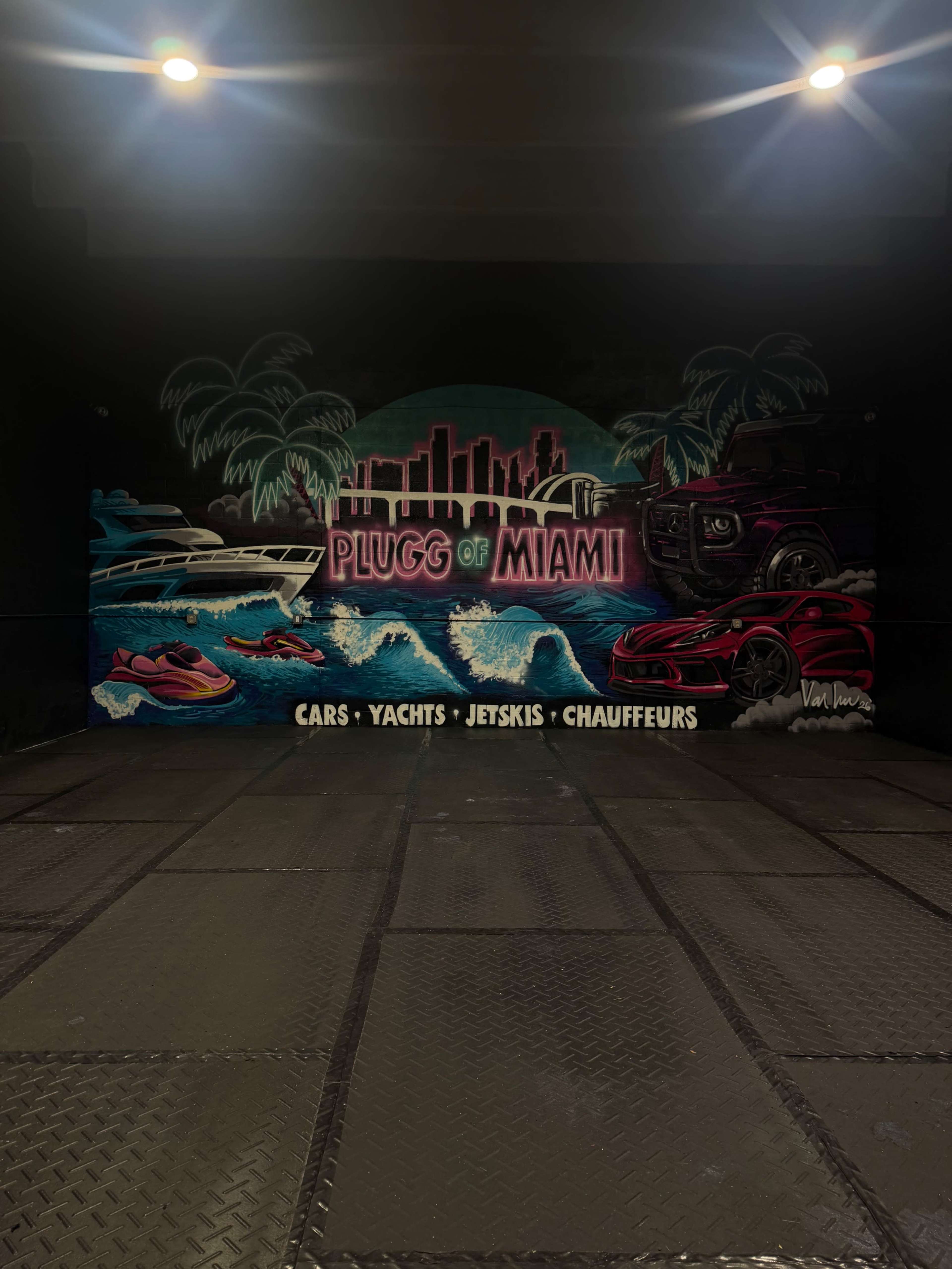 The image shows a vibrant mural featuring the text "PLUGG OF MIAMI" alongside illustrations of boats, jetskis, and a luxury car, set against a backdrop of a city skyline and palm trees.