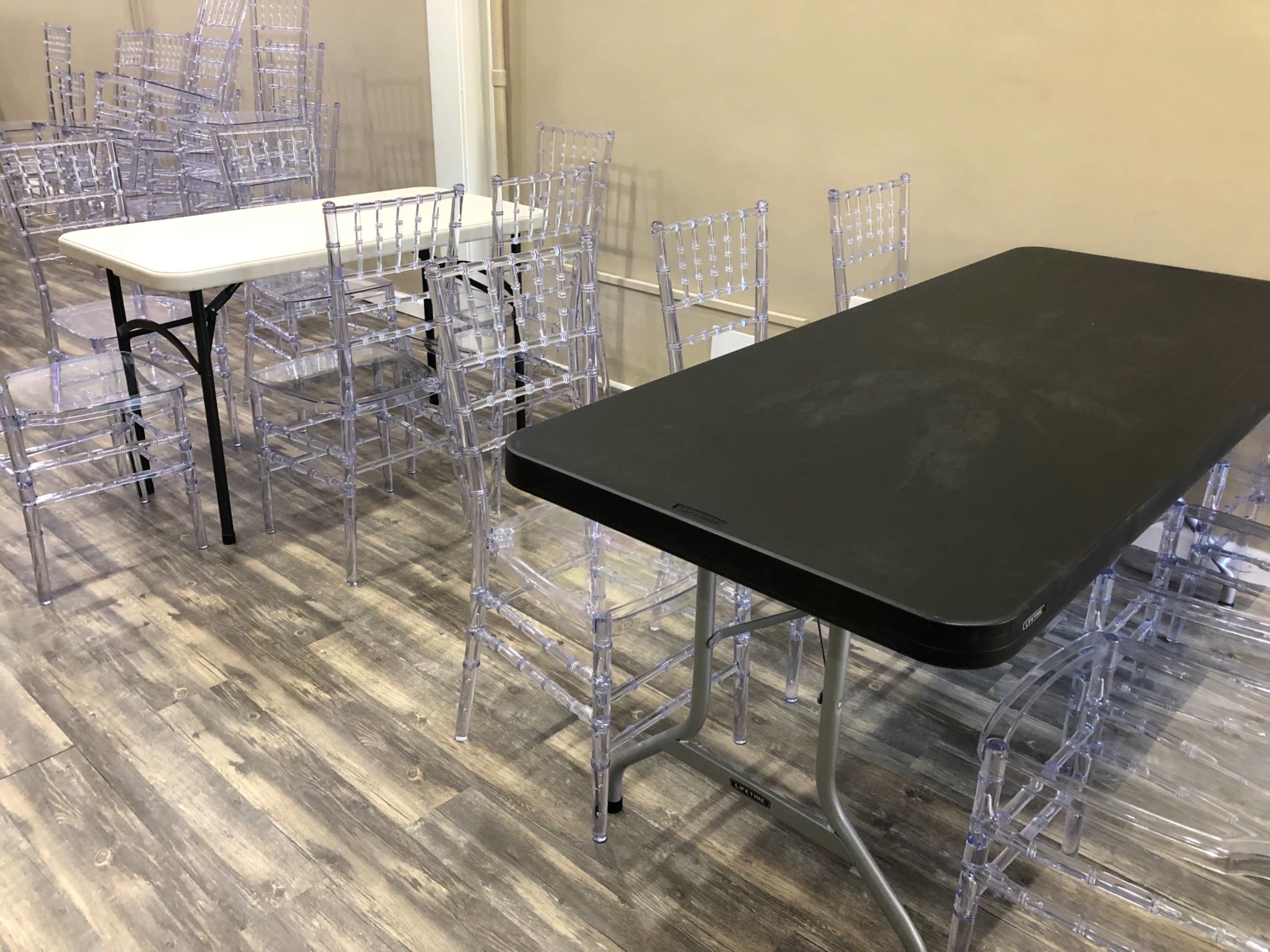 The image shows several transparent plastic chairs arranged around black and white tables in a spacious room.