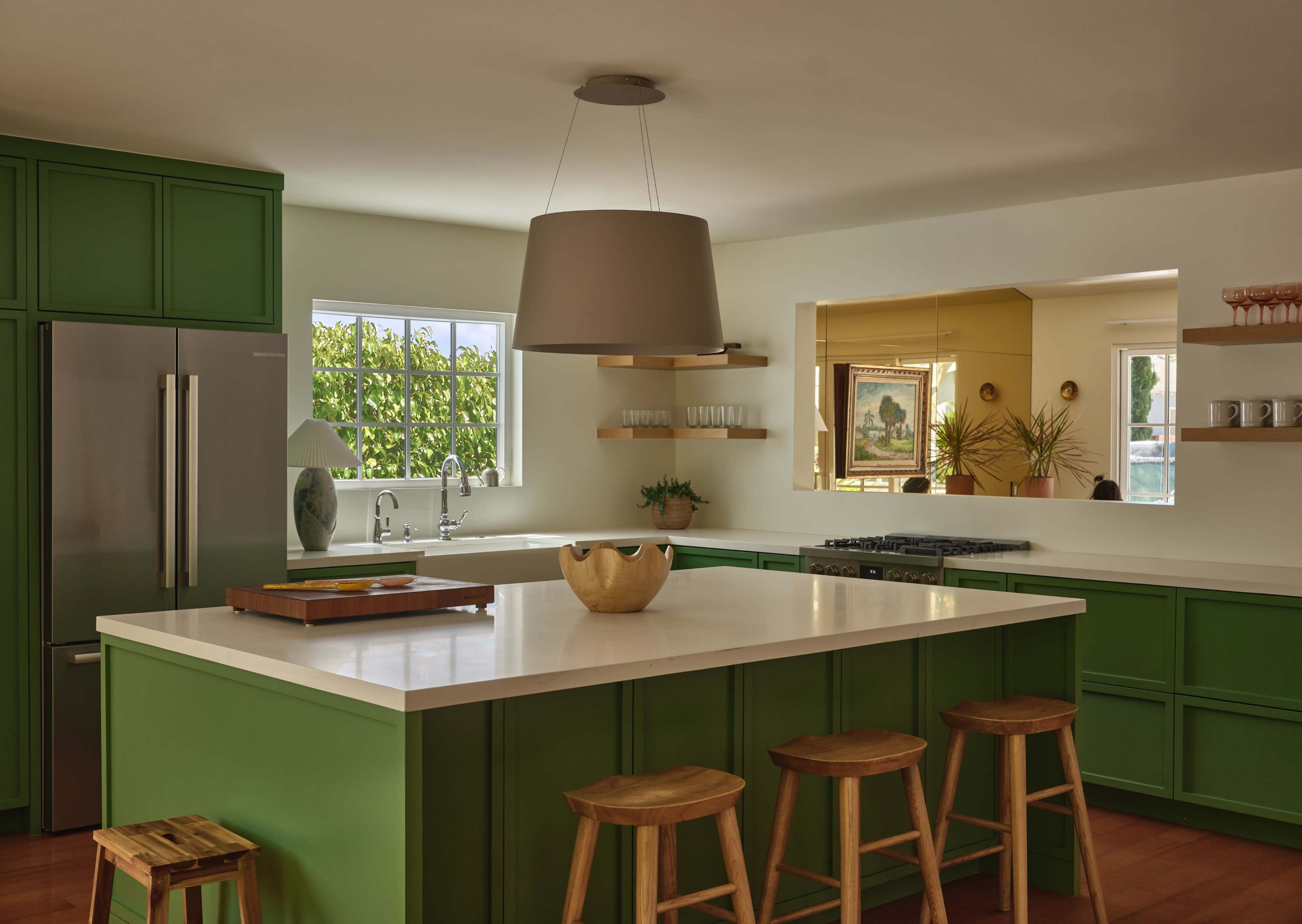 The kitchen features green cabinetry, a large central island with a wooden tray, and modern appliances, with natural light coming through a window.