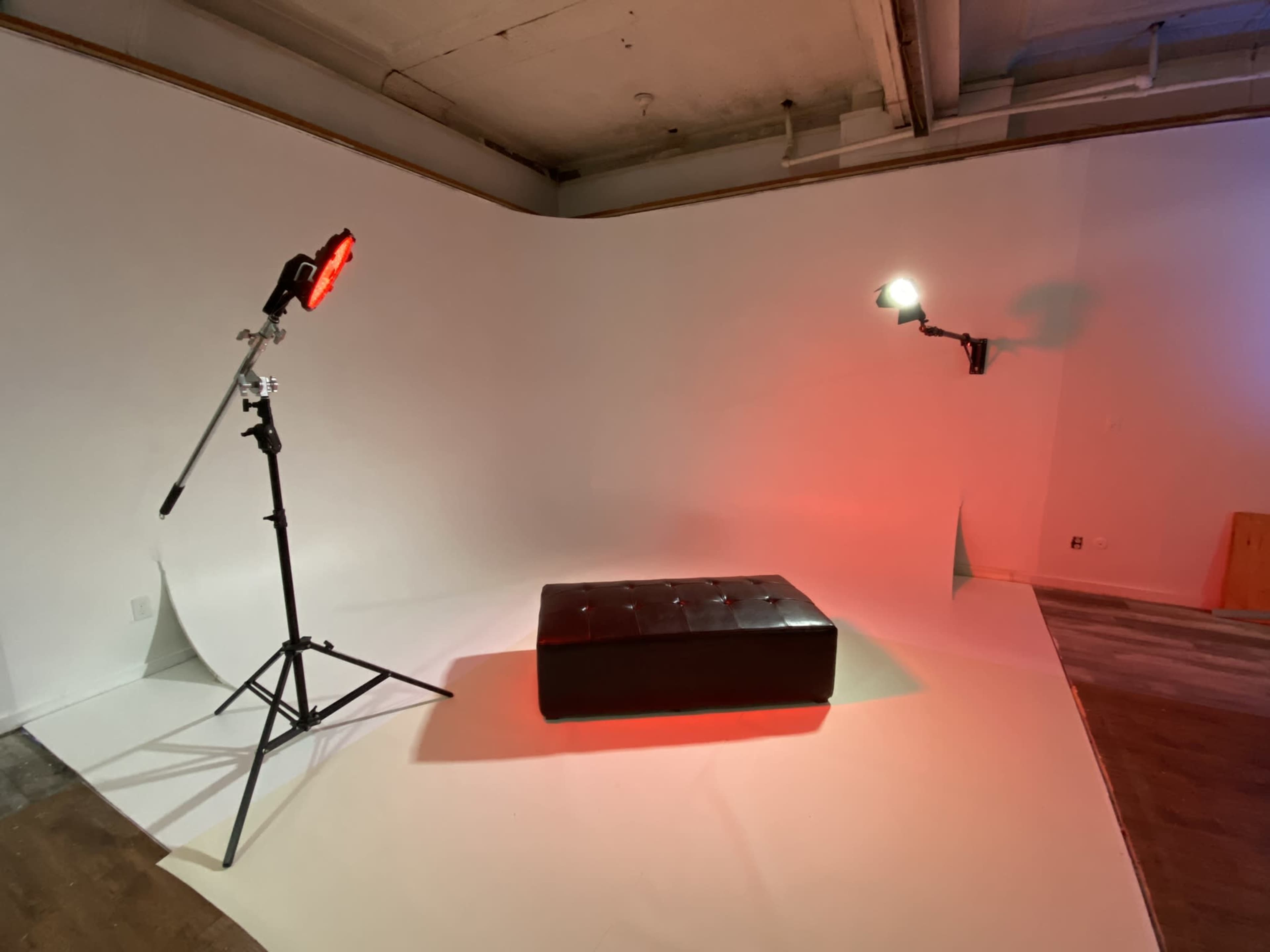 A studio space featuring a black ottoman on a curved white backdrop, illuminated by two lighting stands.