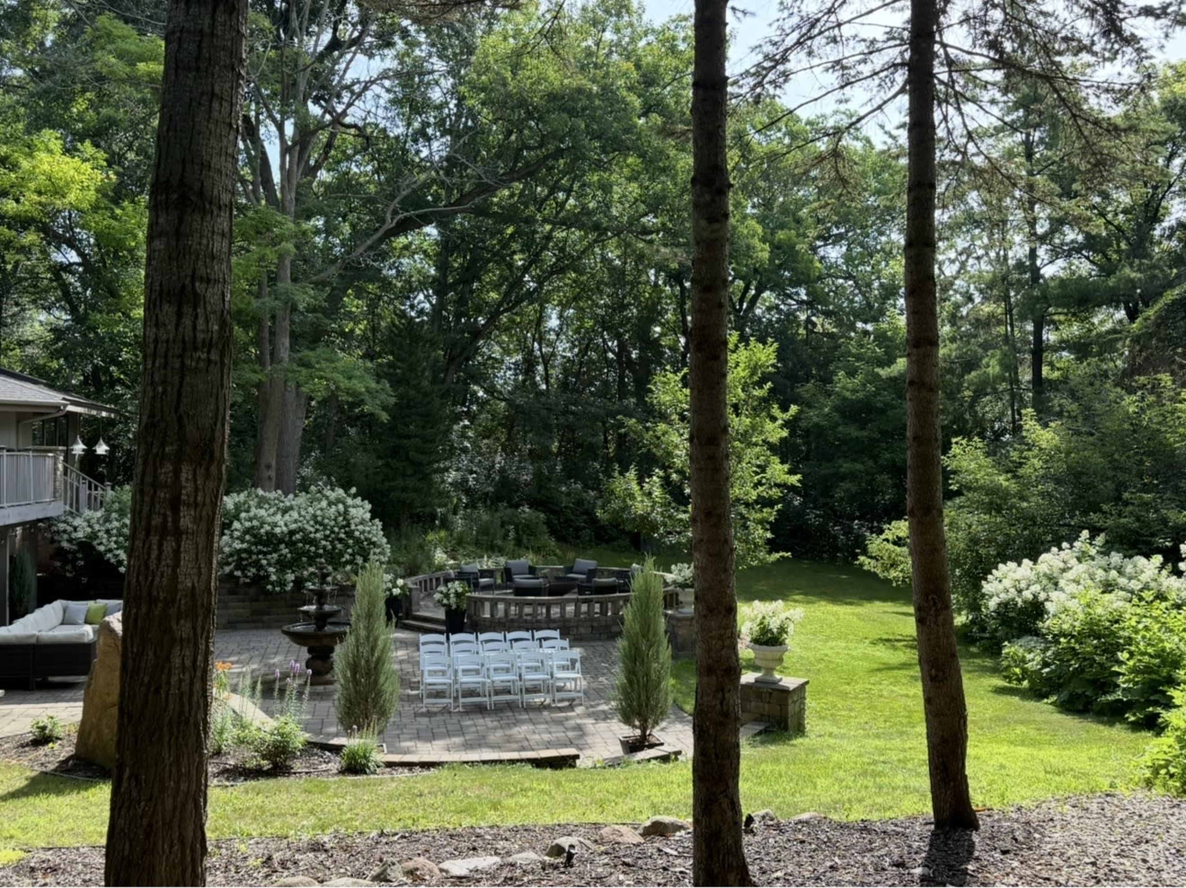 The image shows a backyard area with chairs arranged in rows around a deck, surrounded by trees and shrubs.