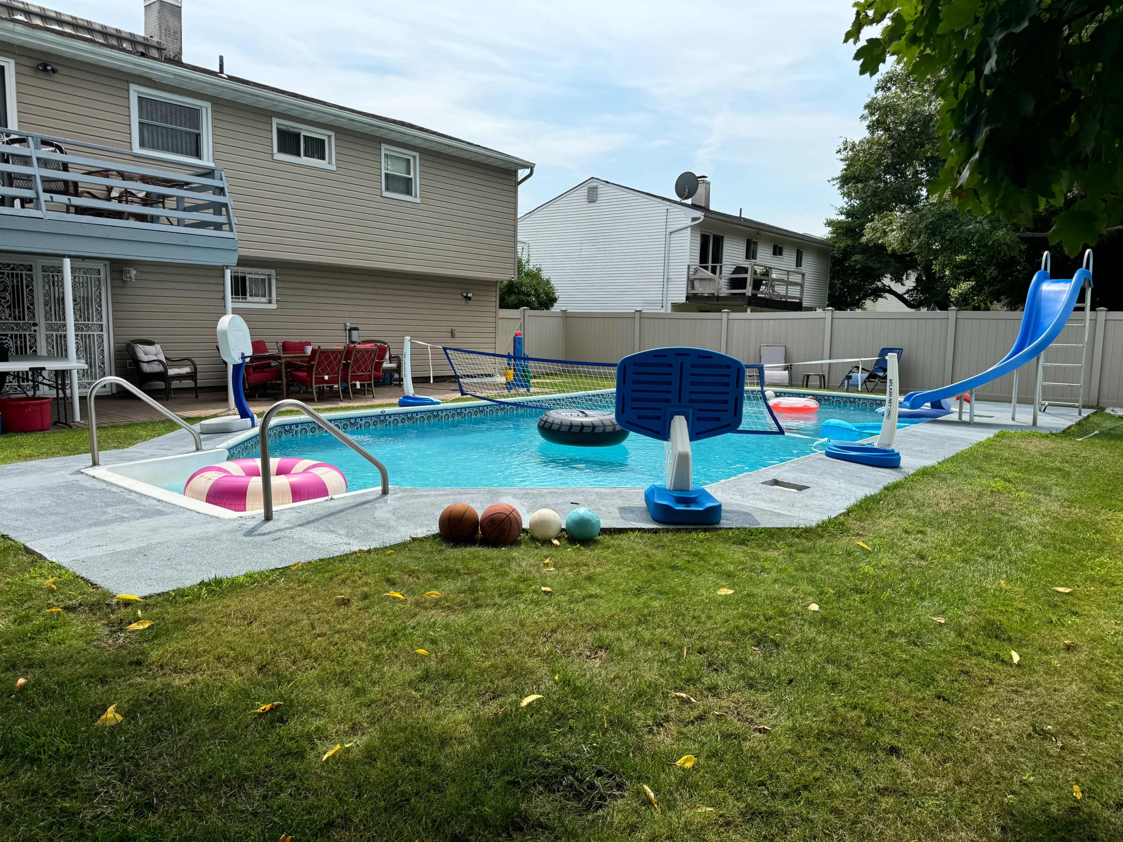 A backyard swimming pool surrounded by grassy areas, featuring various inflatable pool floats and a slide.