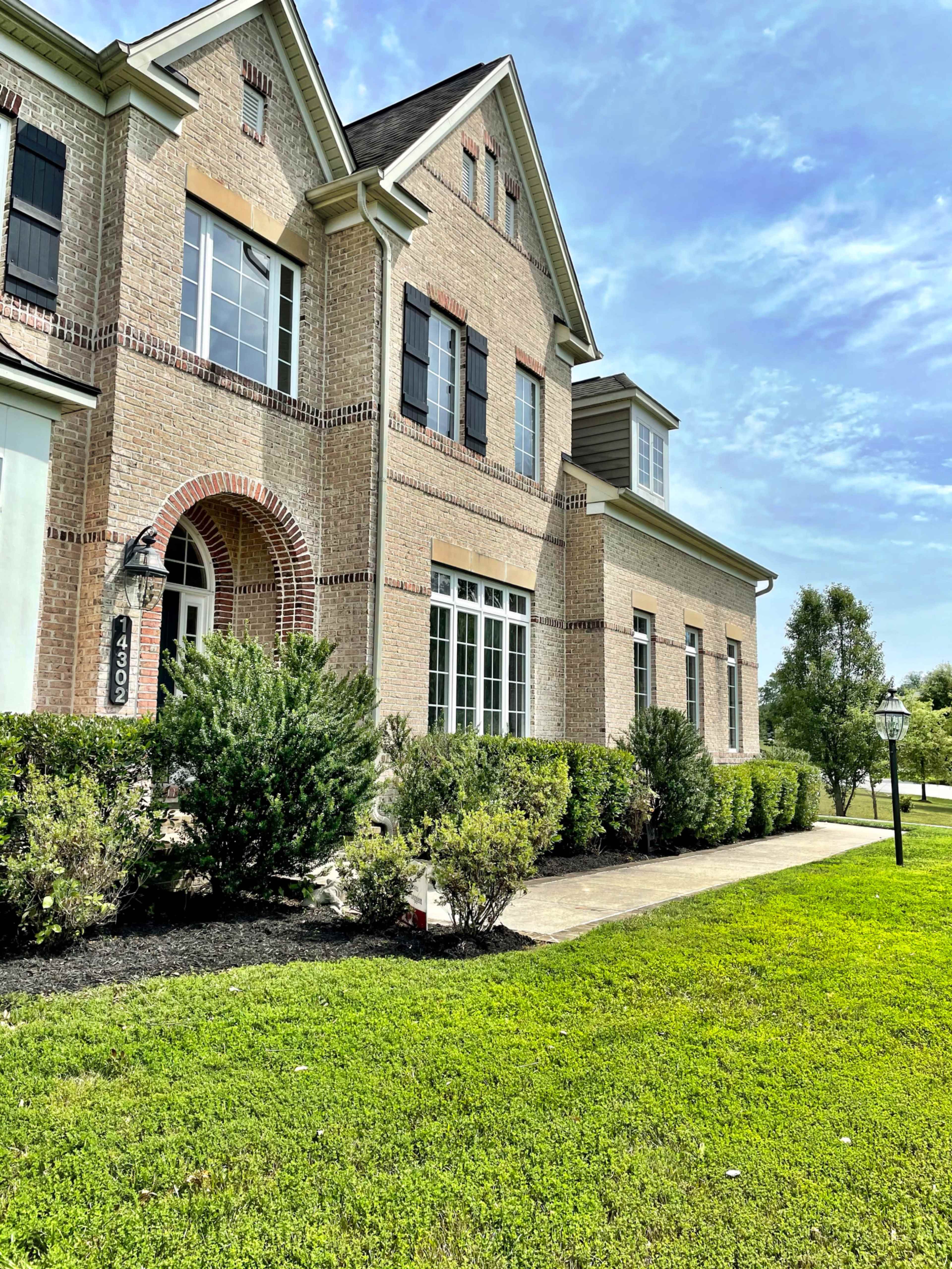 A large brick house with multiple windows and a well-maintained lawn and hedges in front.
