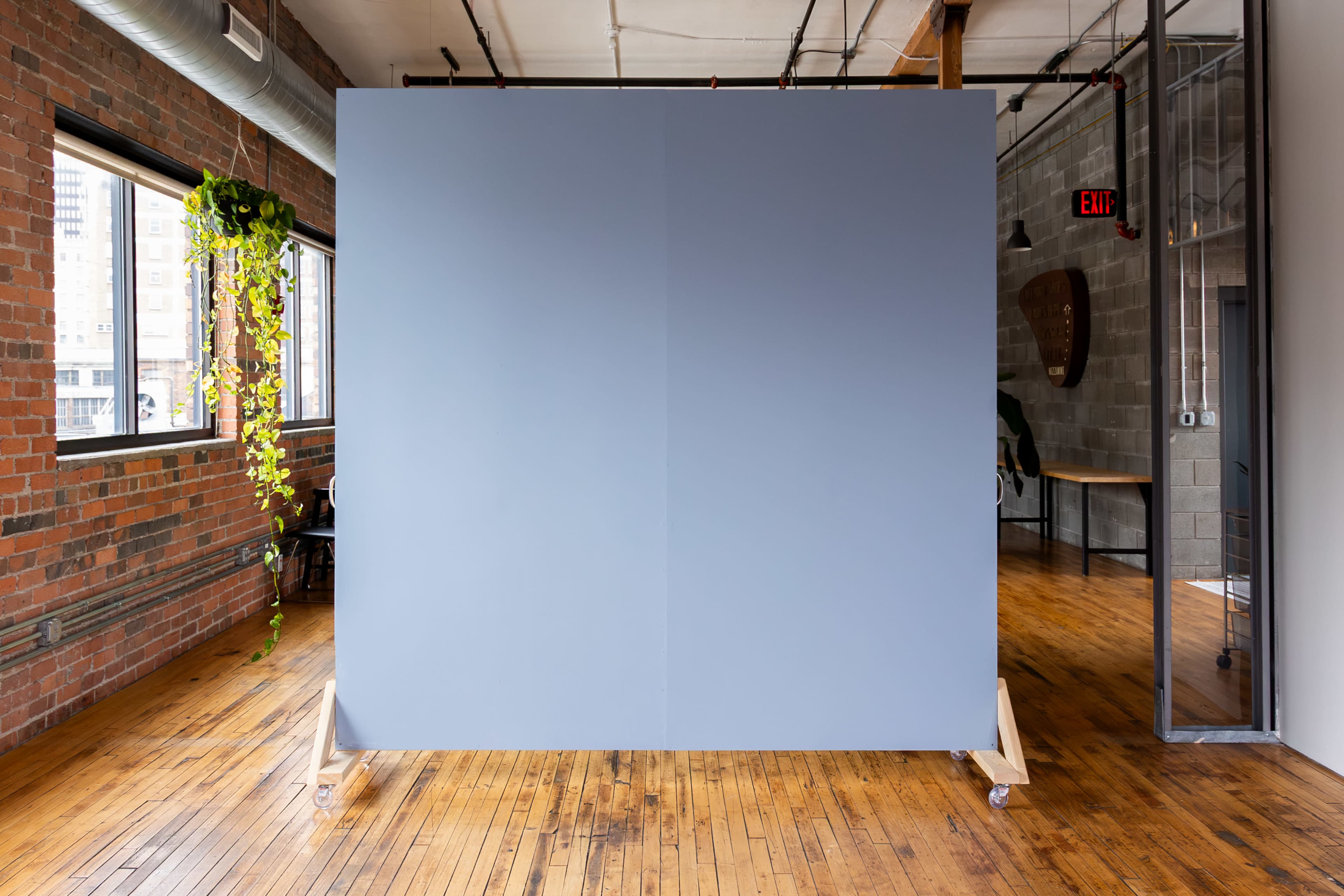 A large gray partition on wheels stands in a spacious room with exposed brick walls and wooden flooring.