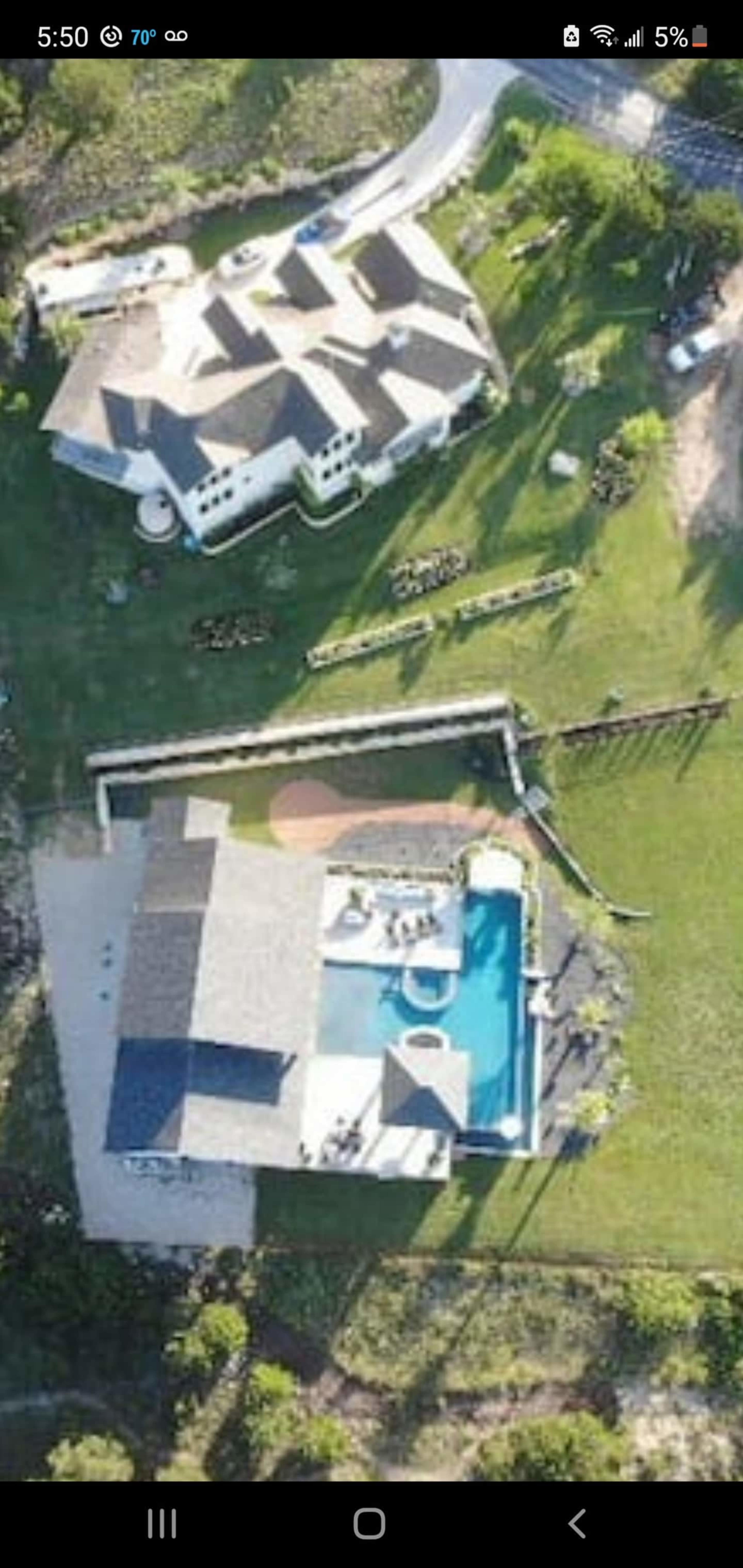 The image shows an aerial view of two large houses set on a green landscape with a swimming pool and a surrounding fence.