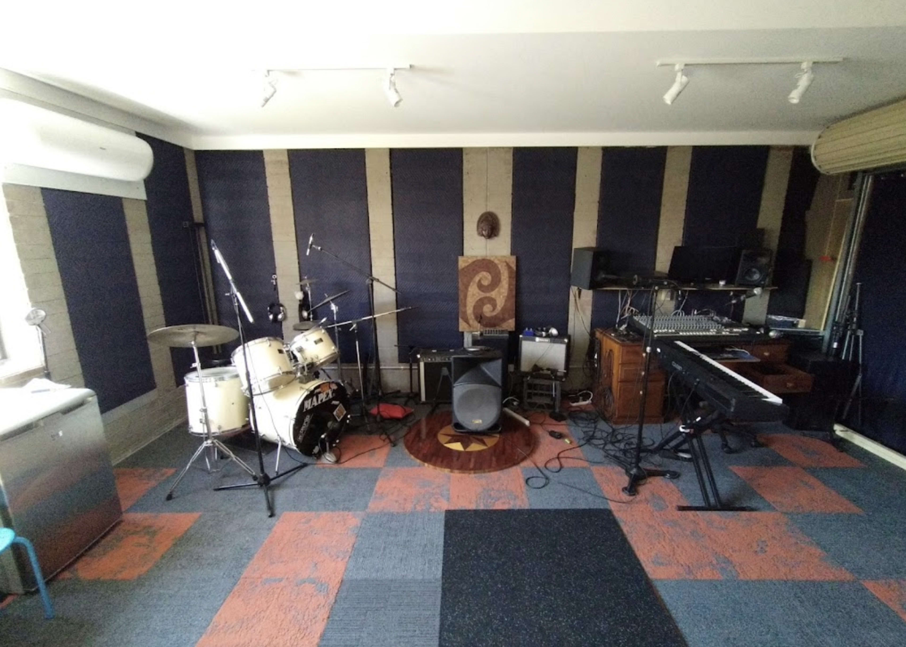 A music studio equipped with a drum set, keyboard, microphones, and various recording equipment arranged in a soundproofed room.