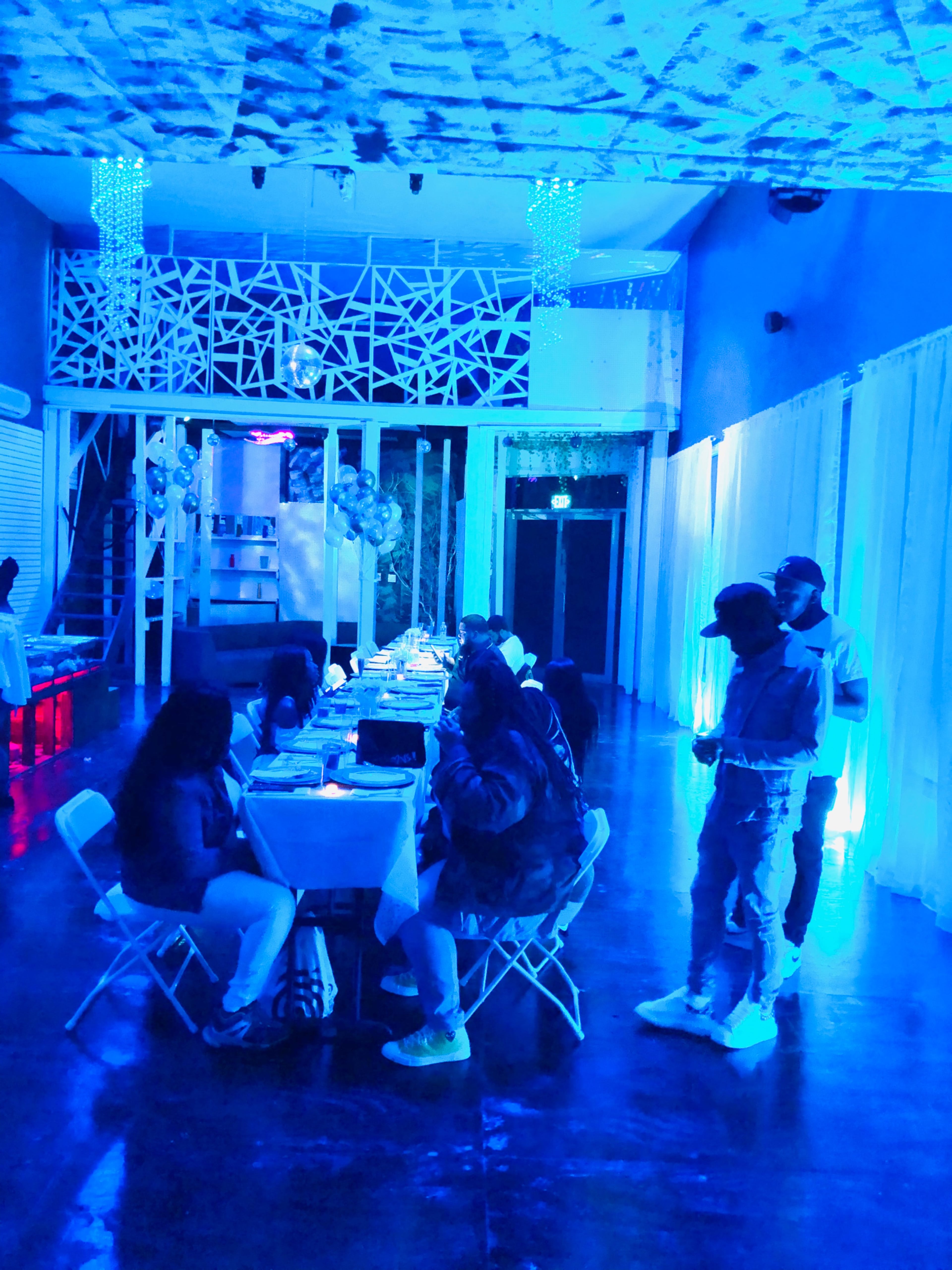 A group of people sits at a table in a dimly lit room adorned with blue lighting and decorative elements.