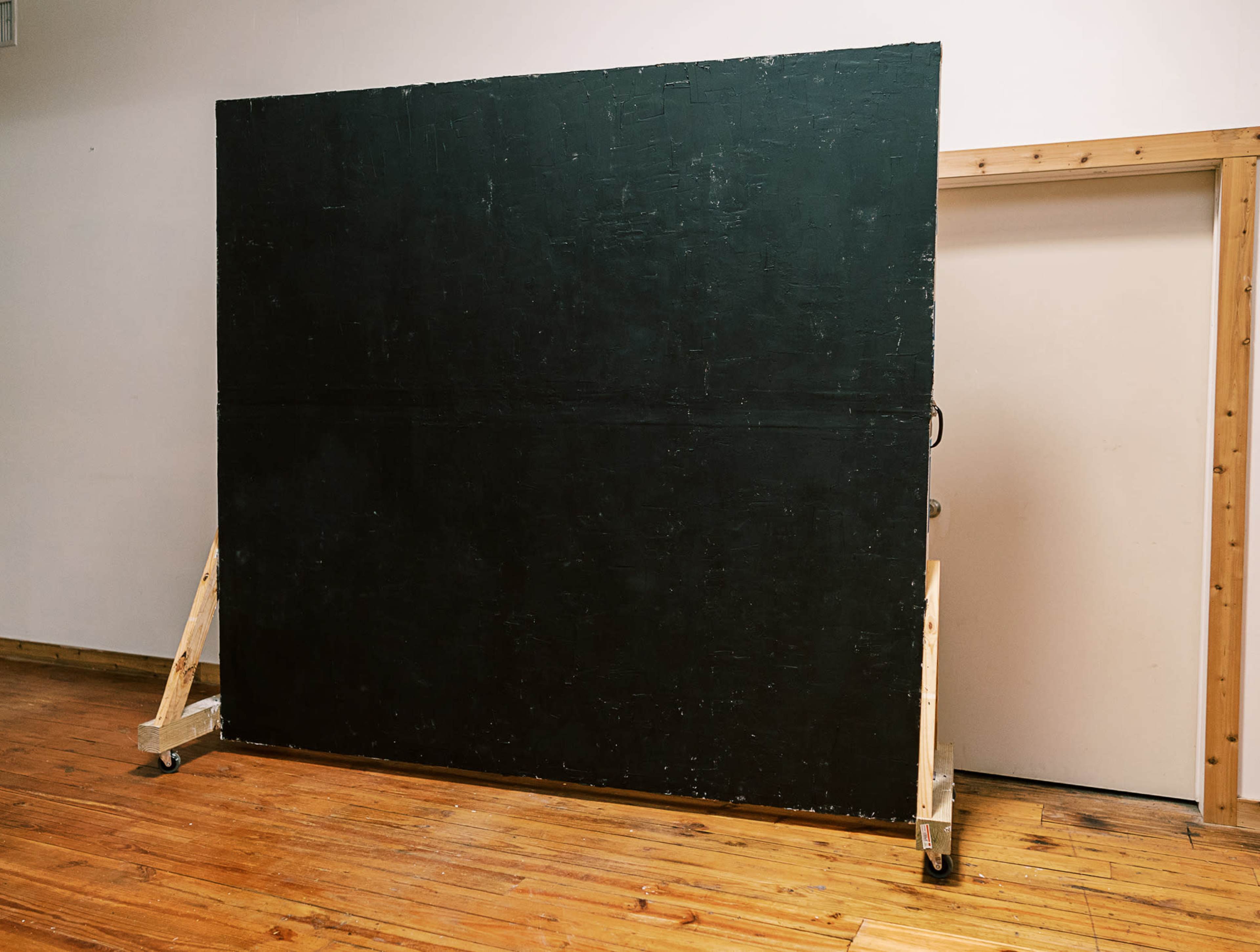 A large black canvas is propped up on wooden stands in an indoor space with wooden flooring.