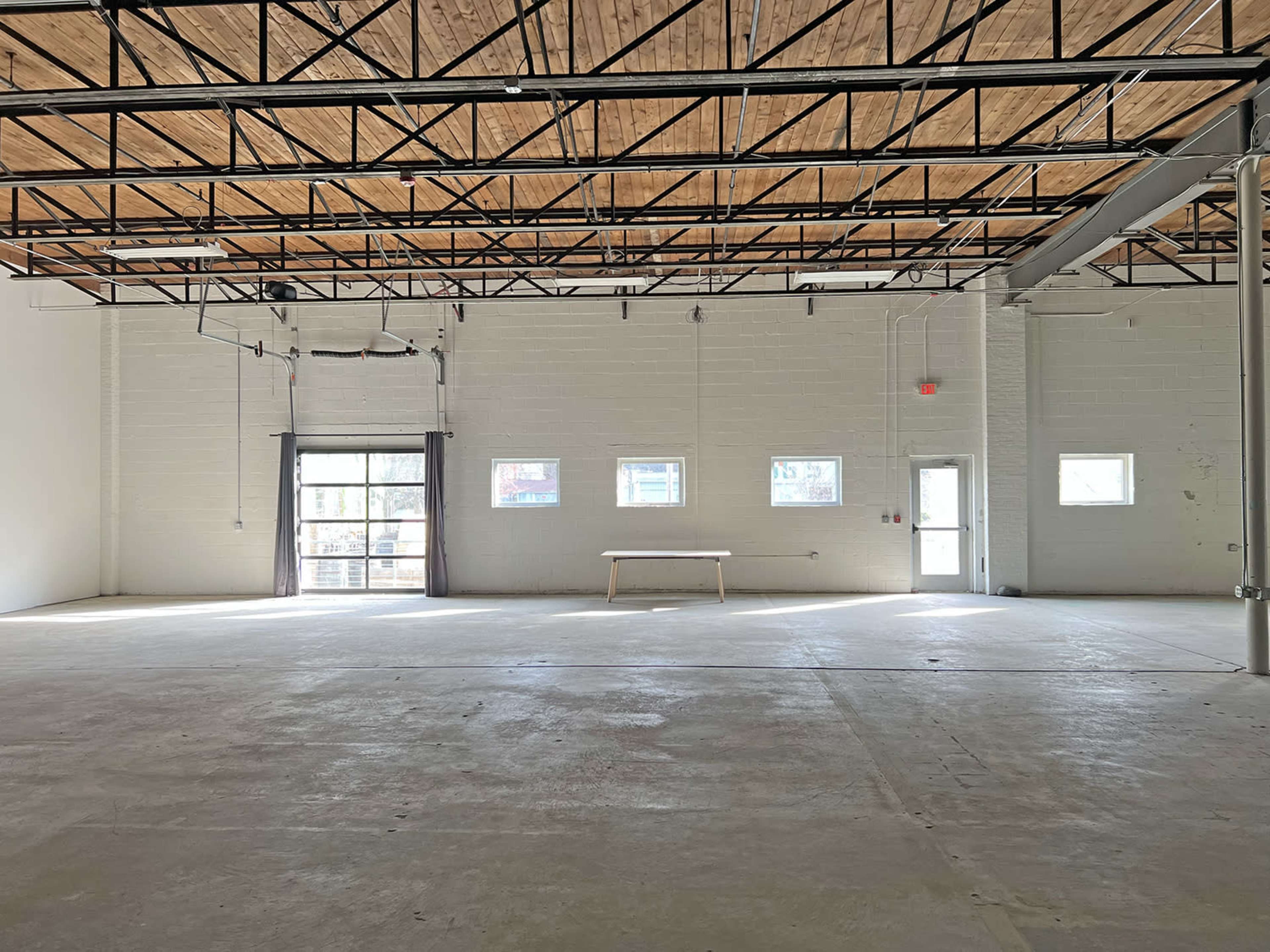 An empty, spacious room with a concrete floor, large windows, and a table positioned in the center.