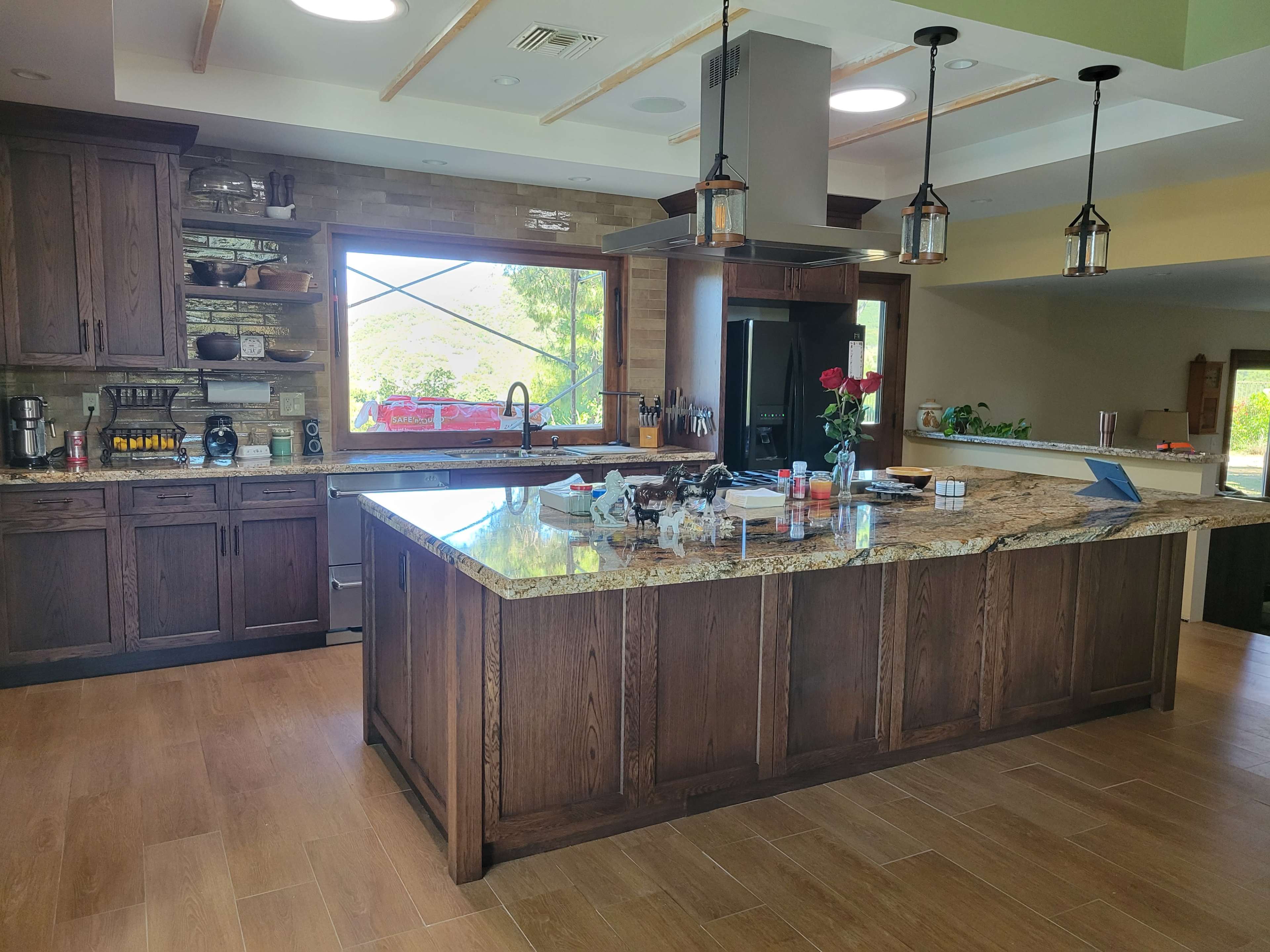 The image shows a spacious kitchen with wooden cabinetry, a large granite island, and modern appliances.