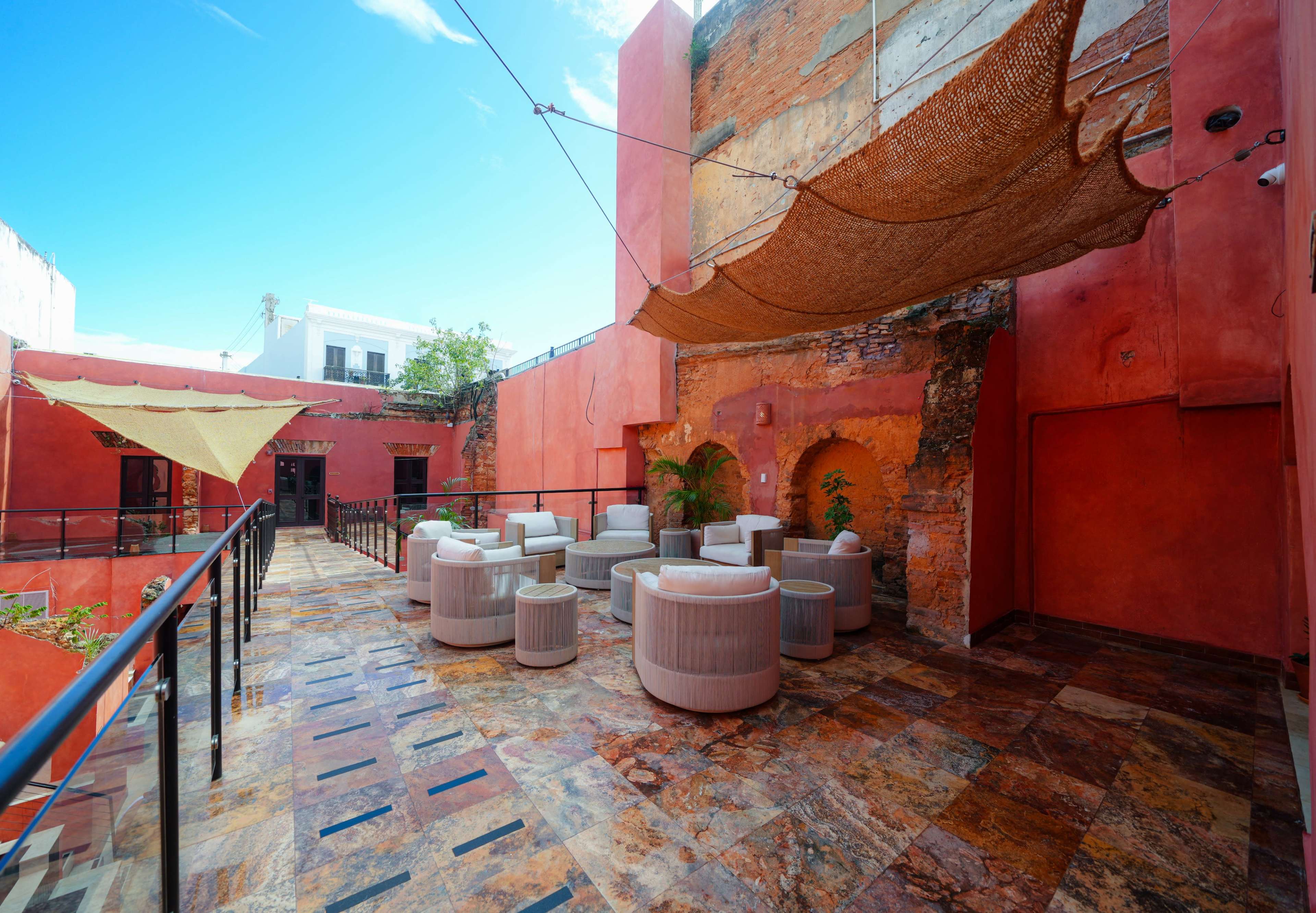 The image shows a bright, open rooftop space with terracotta walls, modern seating arrangements, and decorative netting overhead.