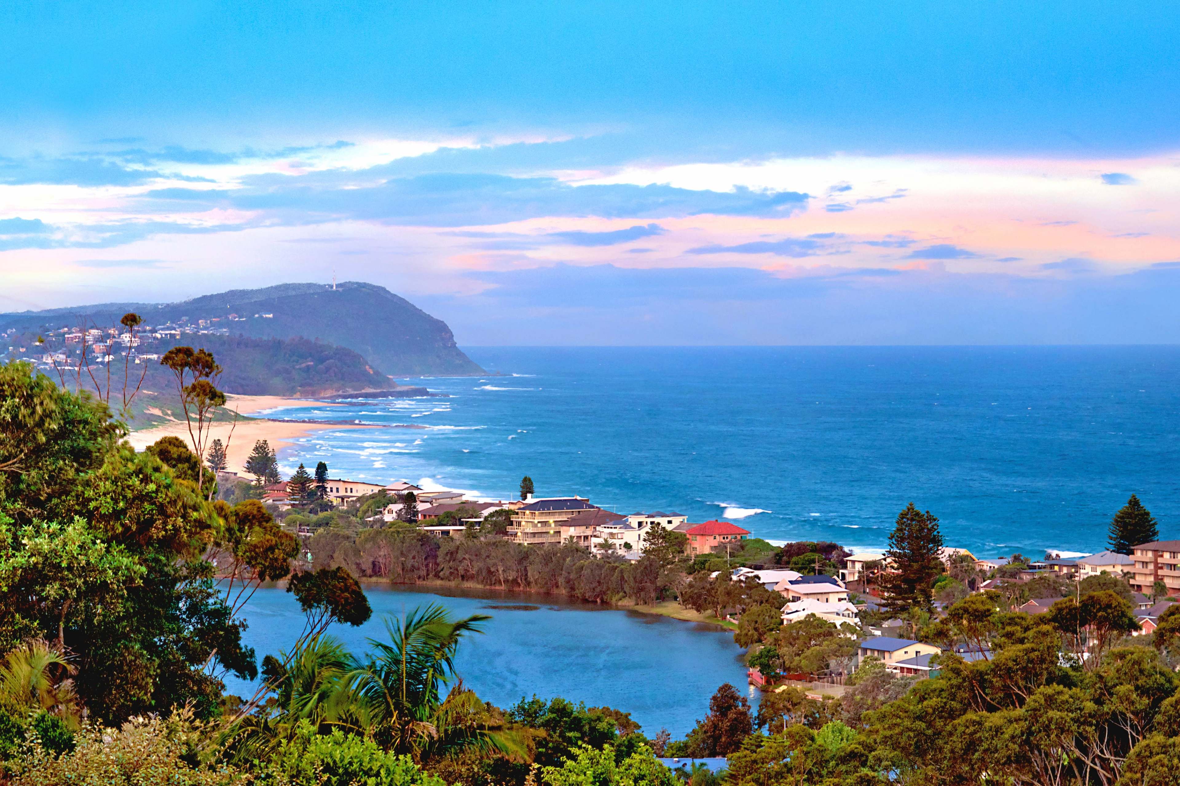 A coastal landscape with rolling waves, a river in the foreground, and hills in the background under a blue sky.