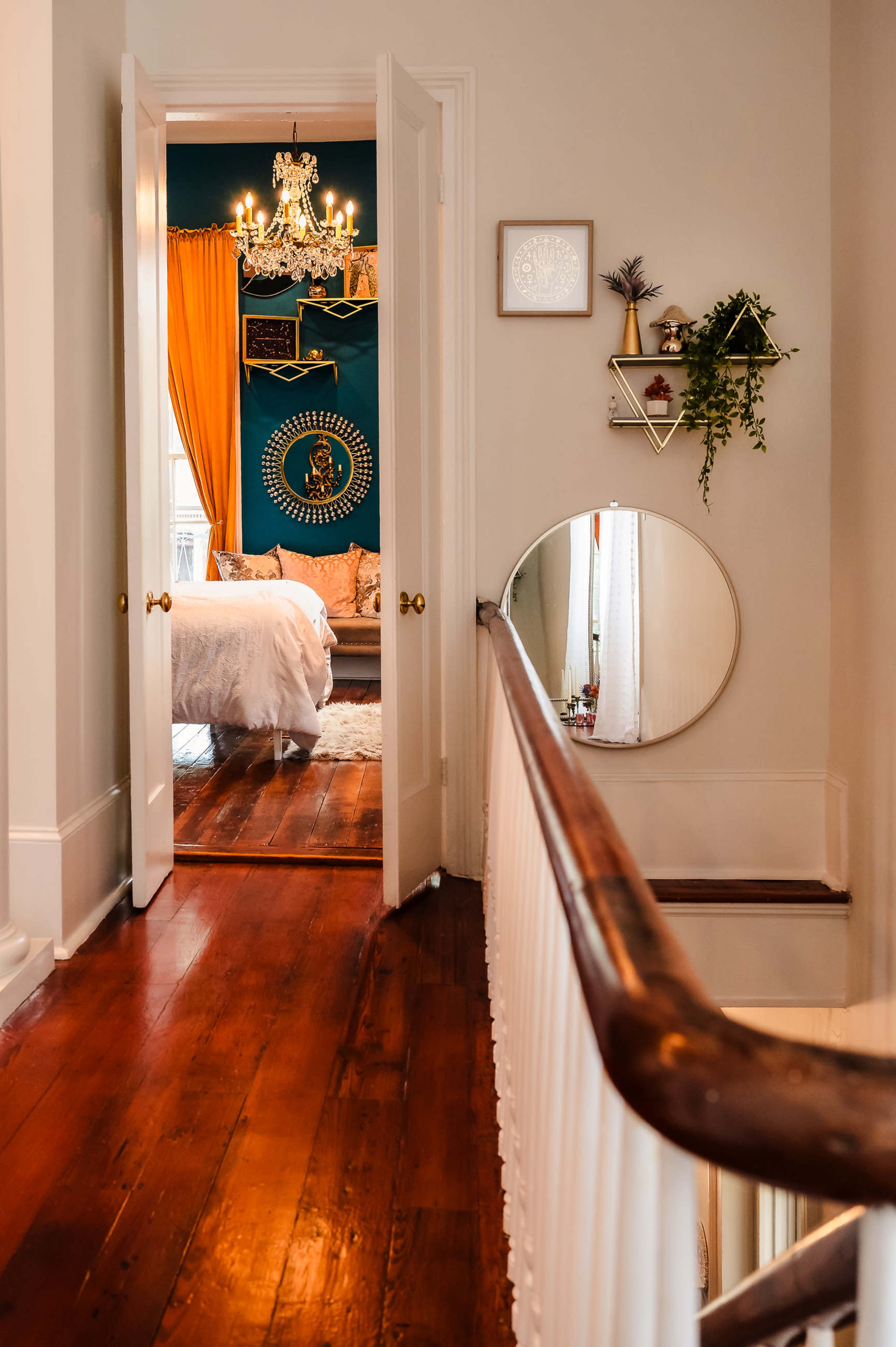 A hallway leads to a bedroom featuring a chandelier, decorative items on the wall, and warm curtains.