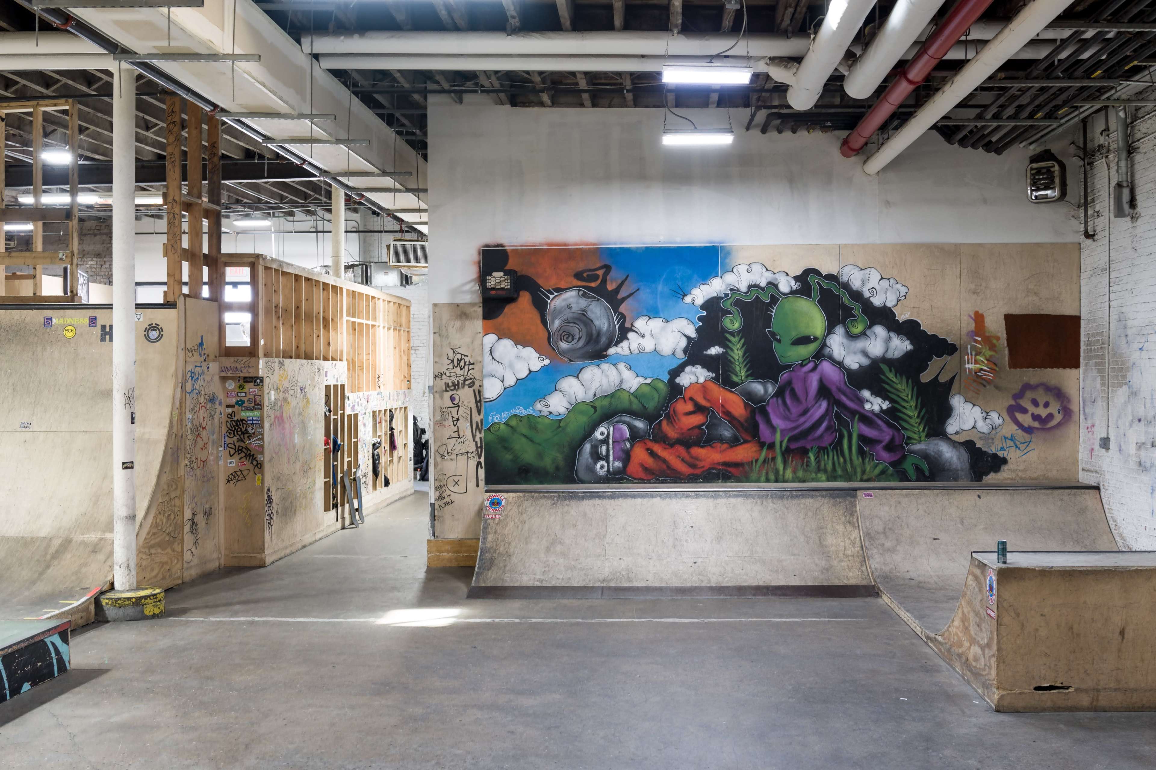 An indoor skatepark featuring ramps and a colorful mural of an alien against a vibrant background.