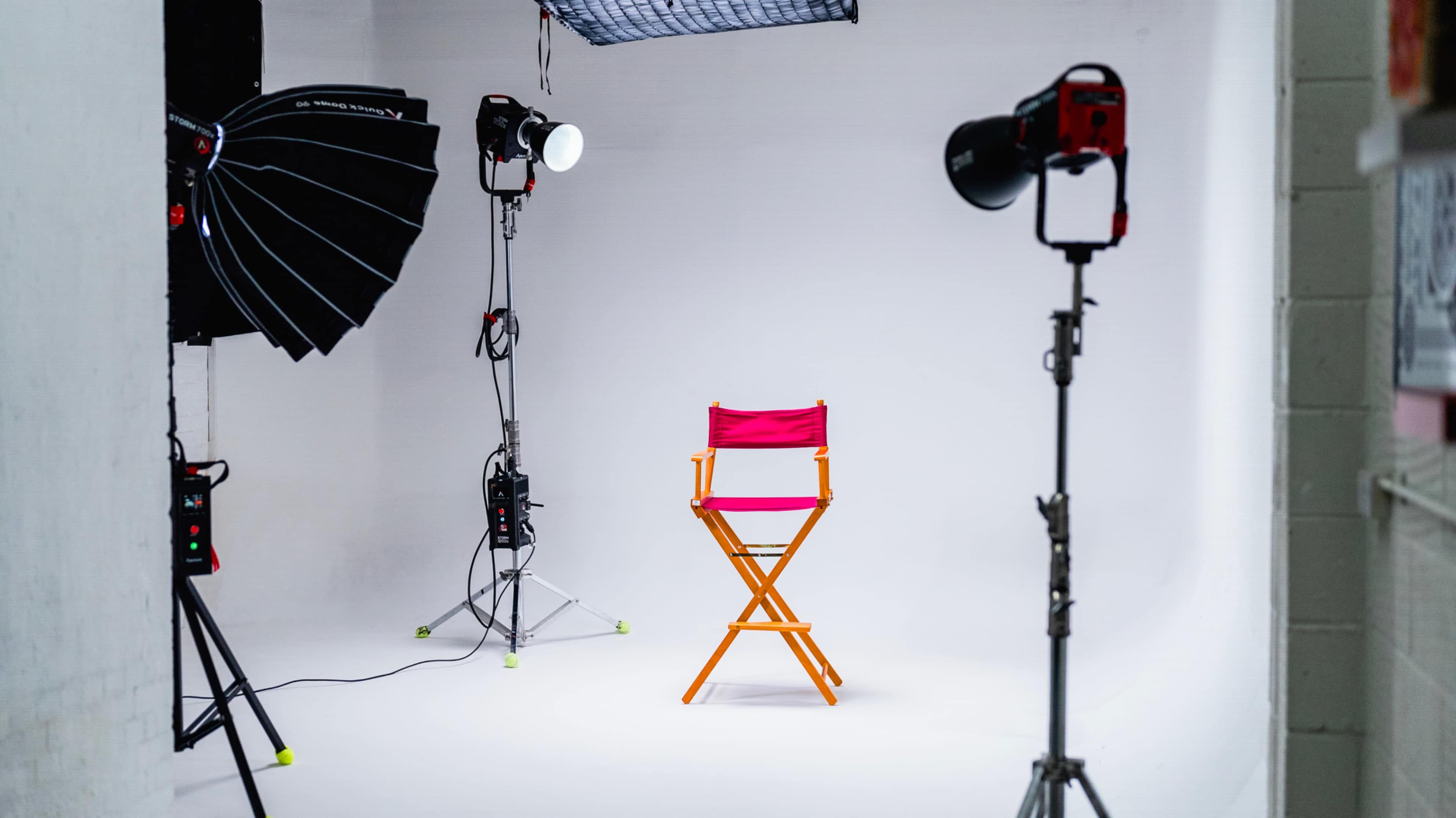 A bright pink director's chair is positioned in a minimalist photo studio surrounded by lighting equipment.